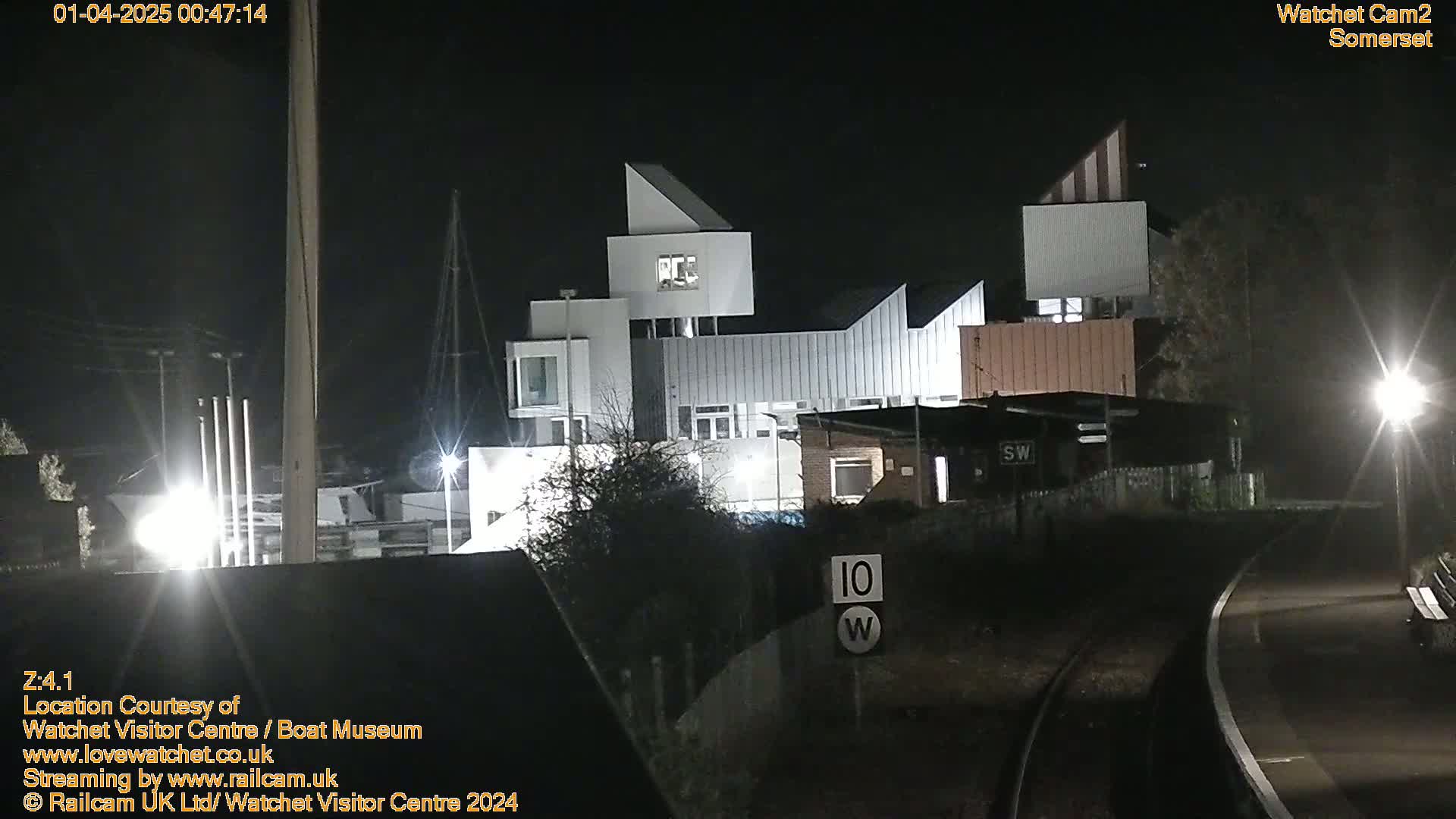 A modern, multi-story building is illuminated at night, near railroad tracks.