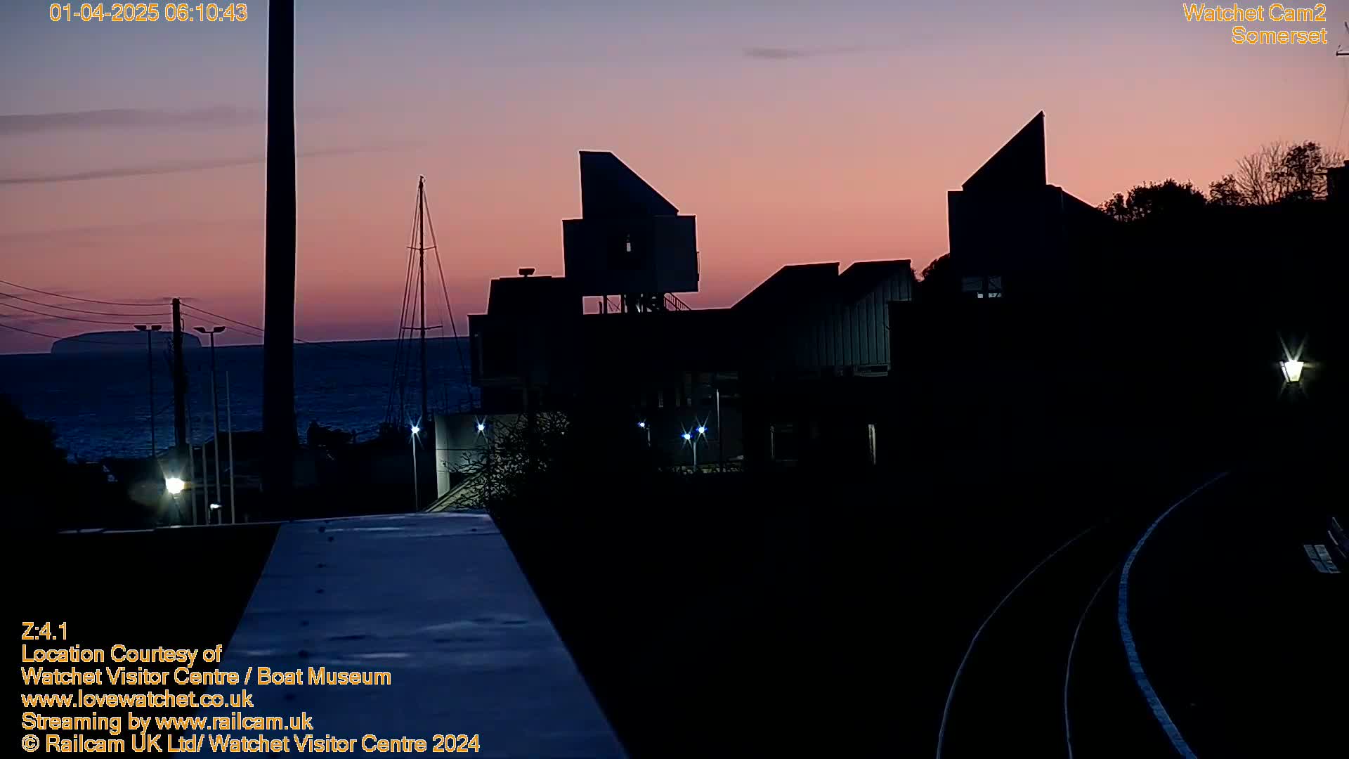 A silhouetted building complex stands against a twilight sky over a calm body of water.