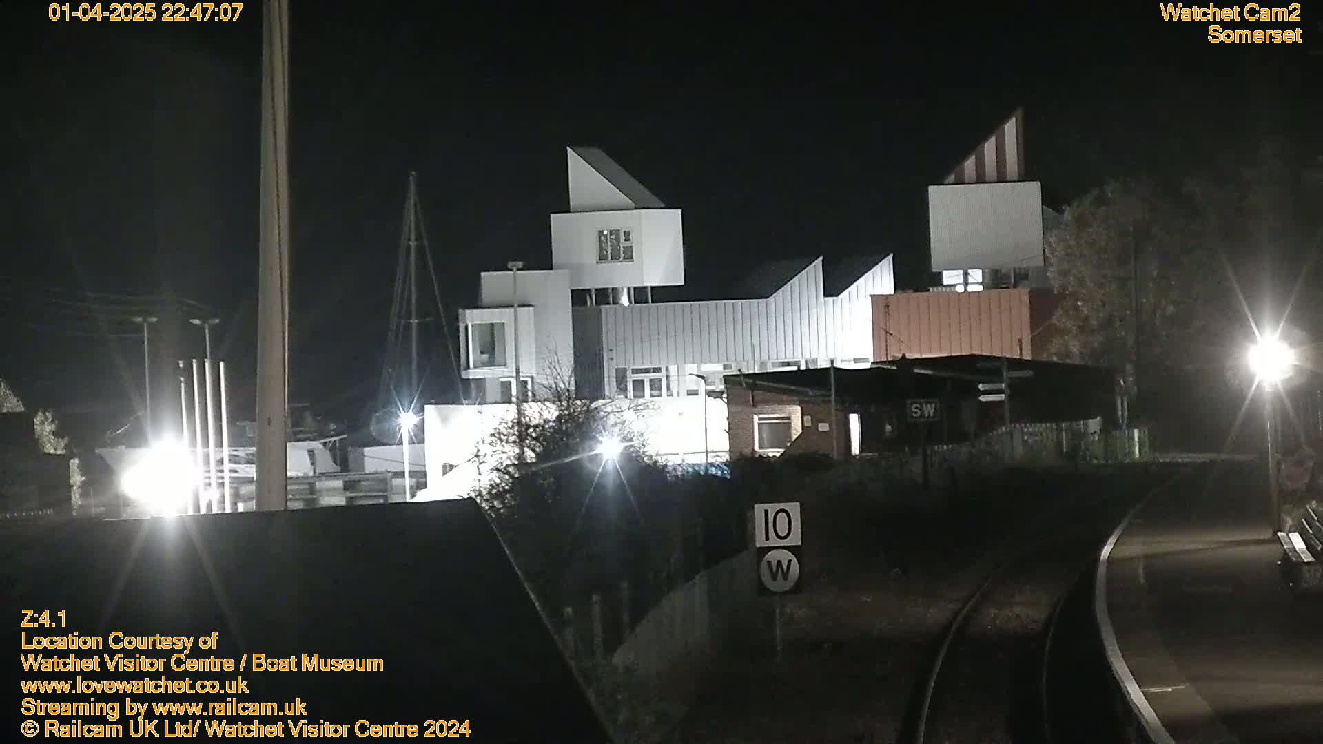 A modern, angular building complex is illuminated at night near a railway track.