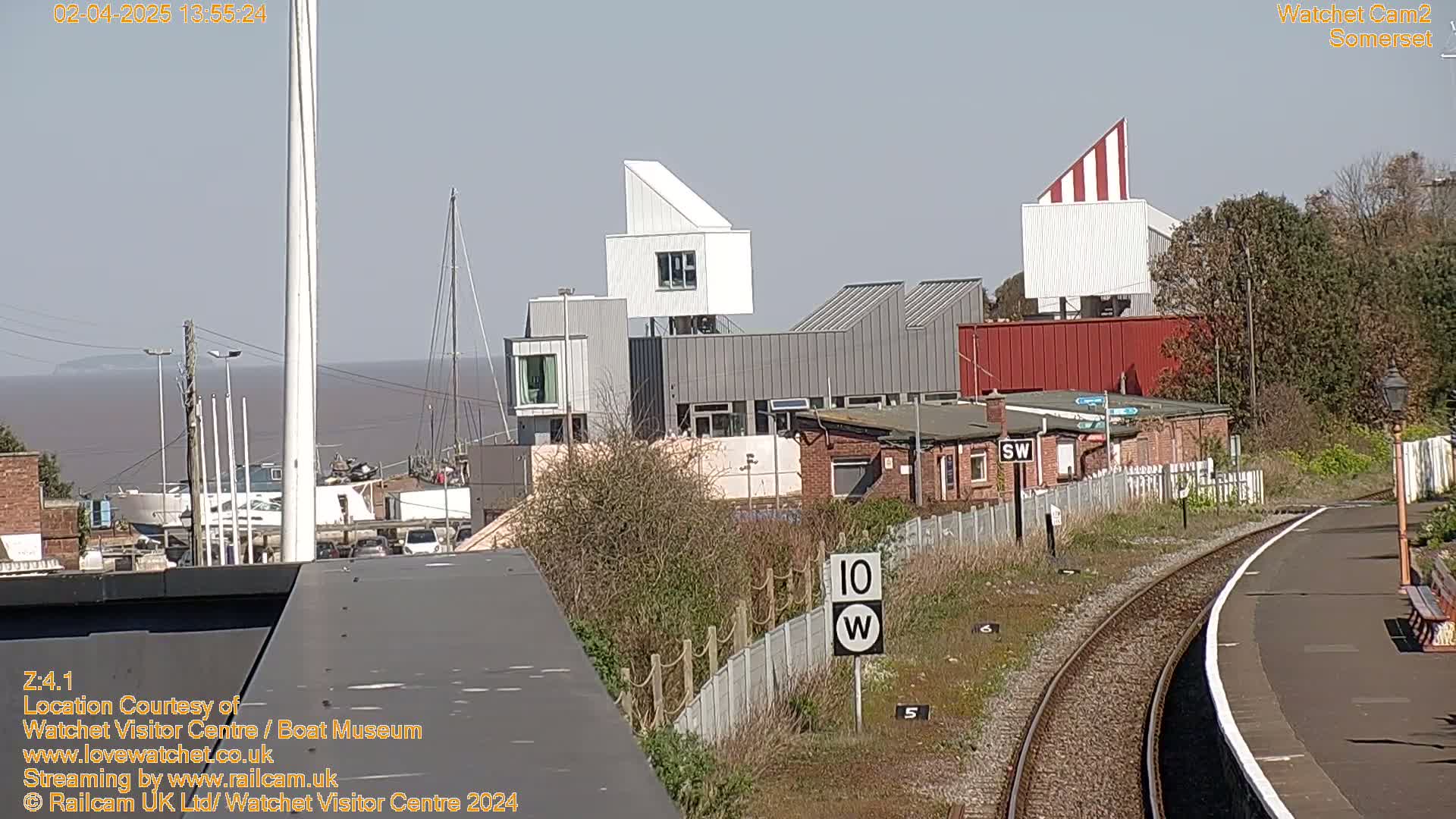 A sunny day shows a harbor with boats, modern buildings, and train tracks curving to the right.