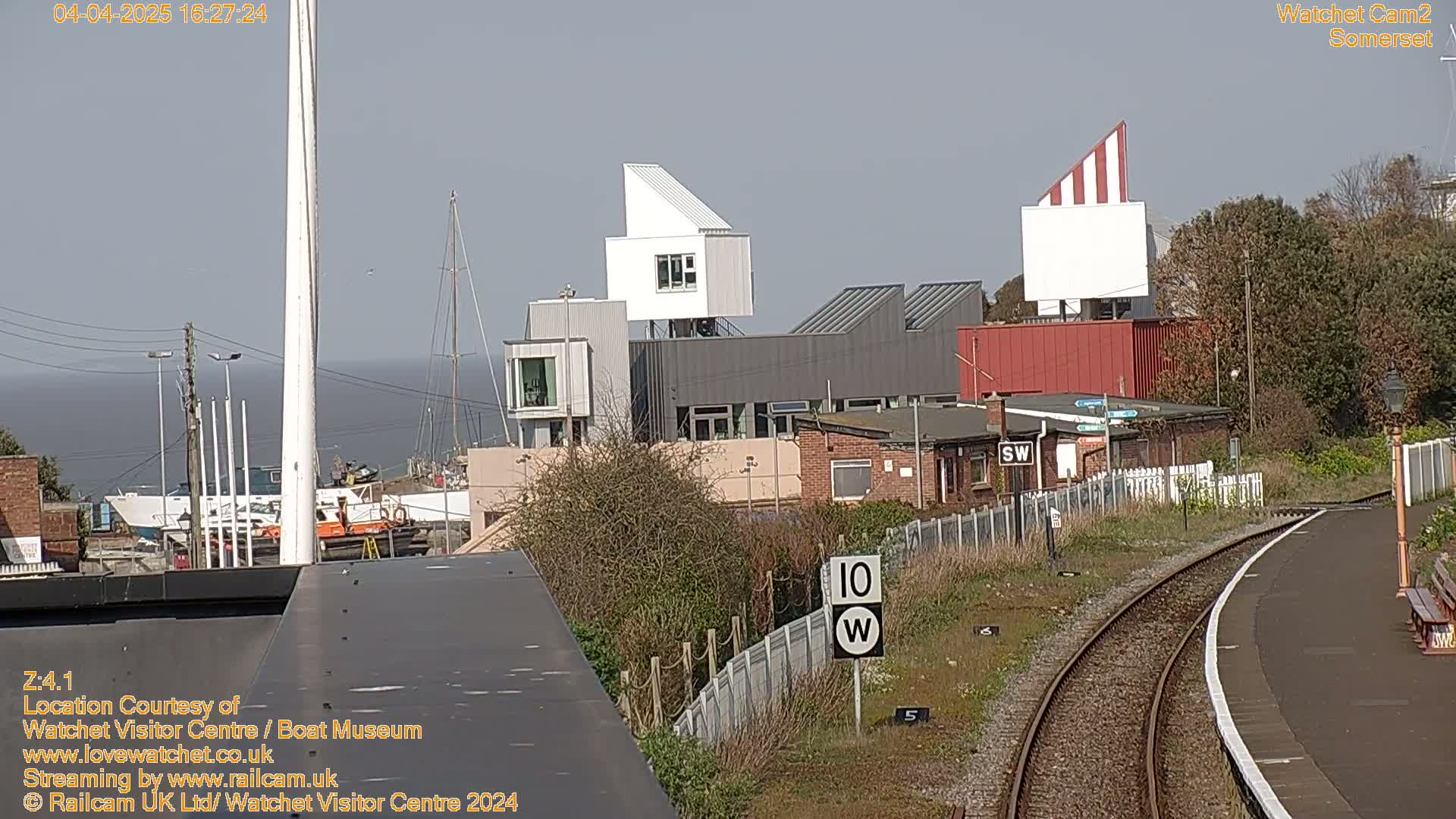 A waterfront scene on a sunny day shows a collection of buildings near a train track and harbor with boats.