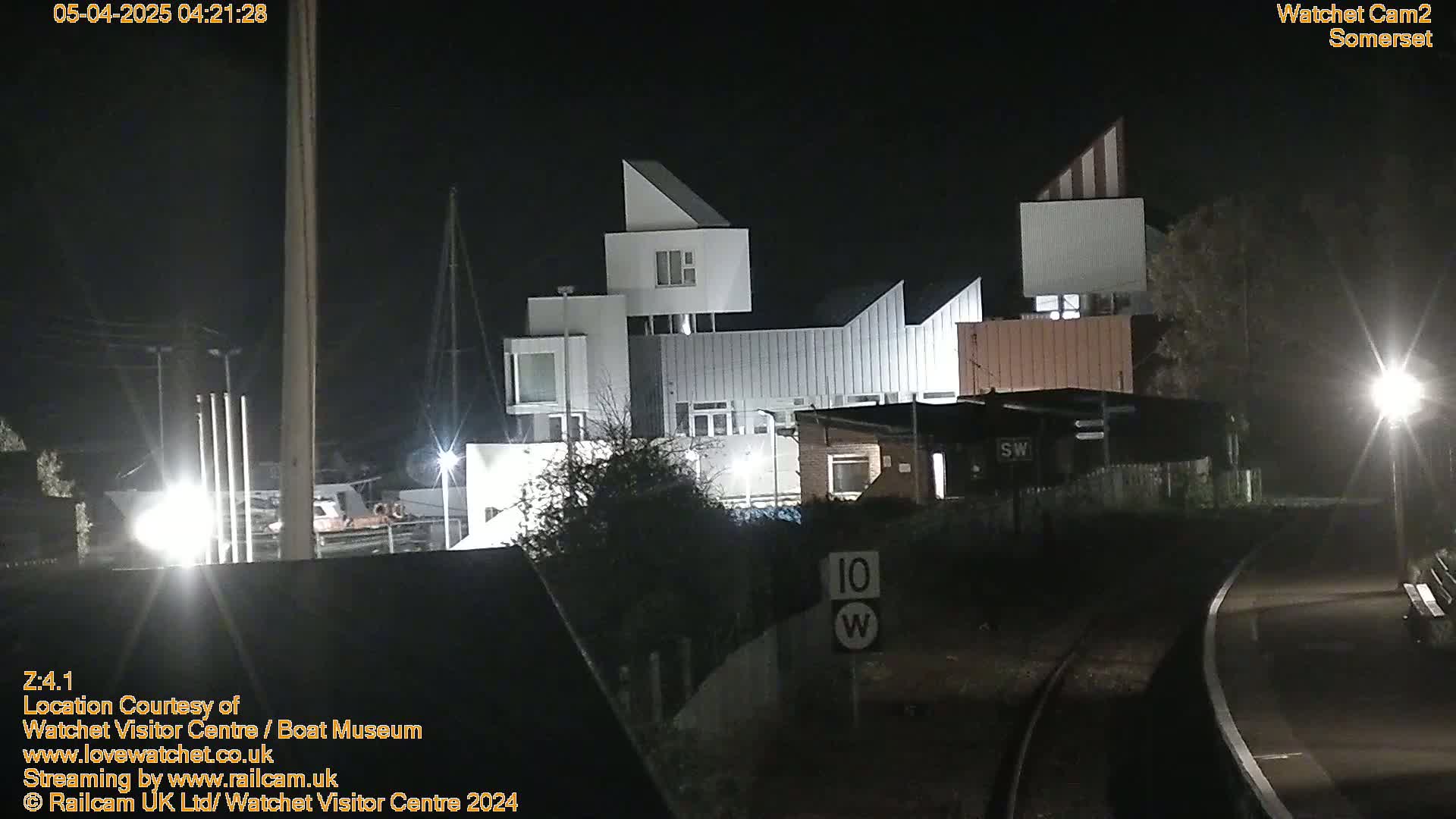 A modern, multi-level building is illuminated at night near railroad tracks under a dark sky.