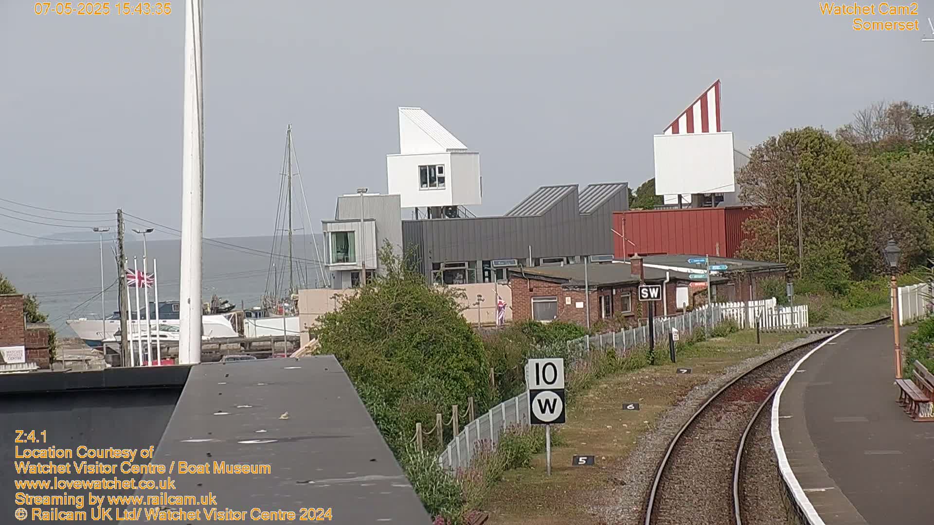 A harbor with boats and modern buildings is seen from a vantage point overlooking train tracks on a sunny day.