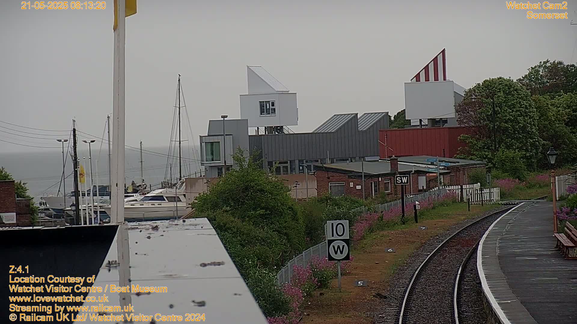 A cloudy day overlooking a harbor with boats, modern buildings, and a train track.