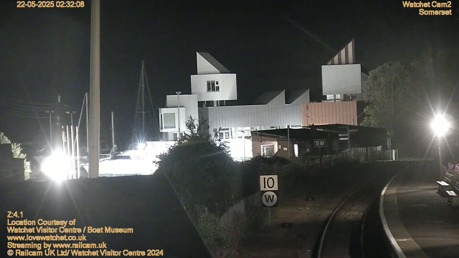 A modern, white building complex is illuminated at night near a railway track under a dark sky.
