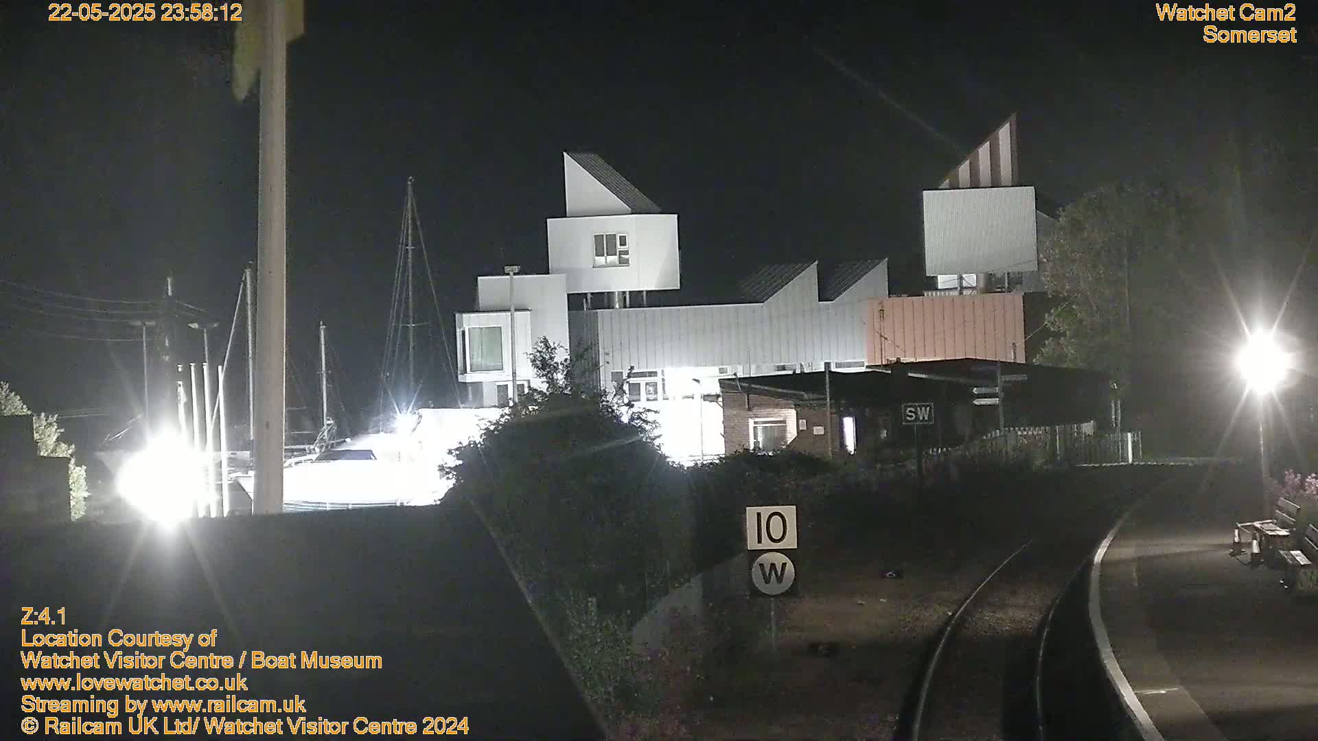 A modern, multi-story building is illuminated at night near a railway line under clear skies.