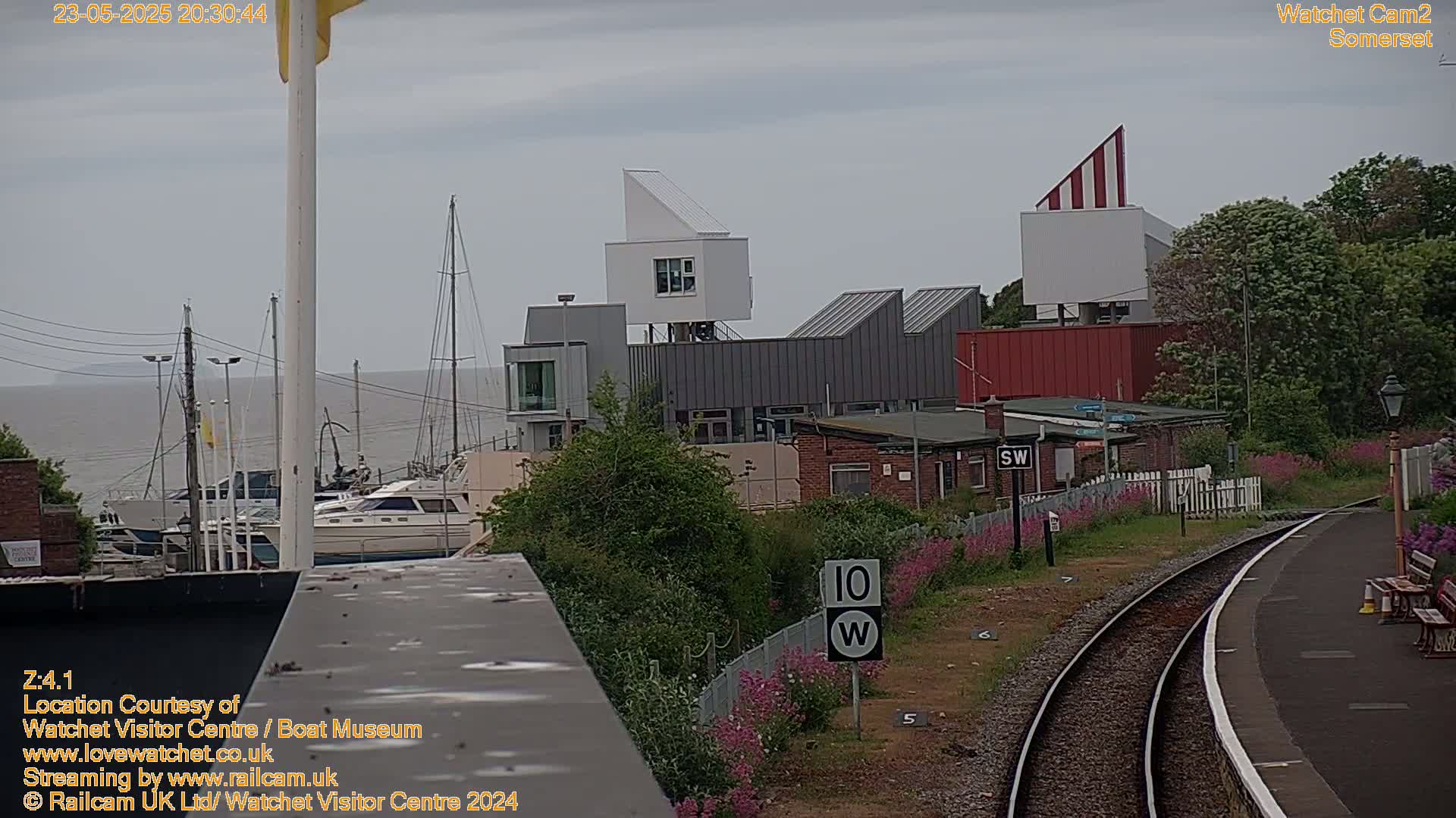 A view of a harbor with boats, modern buildings, and a railway track, under an overcast sky.
