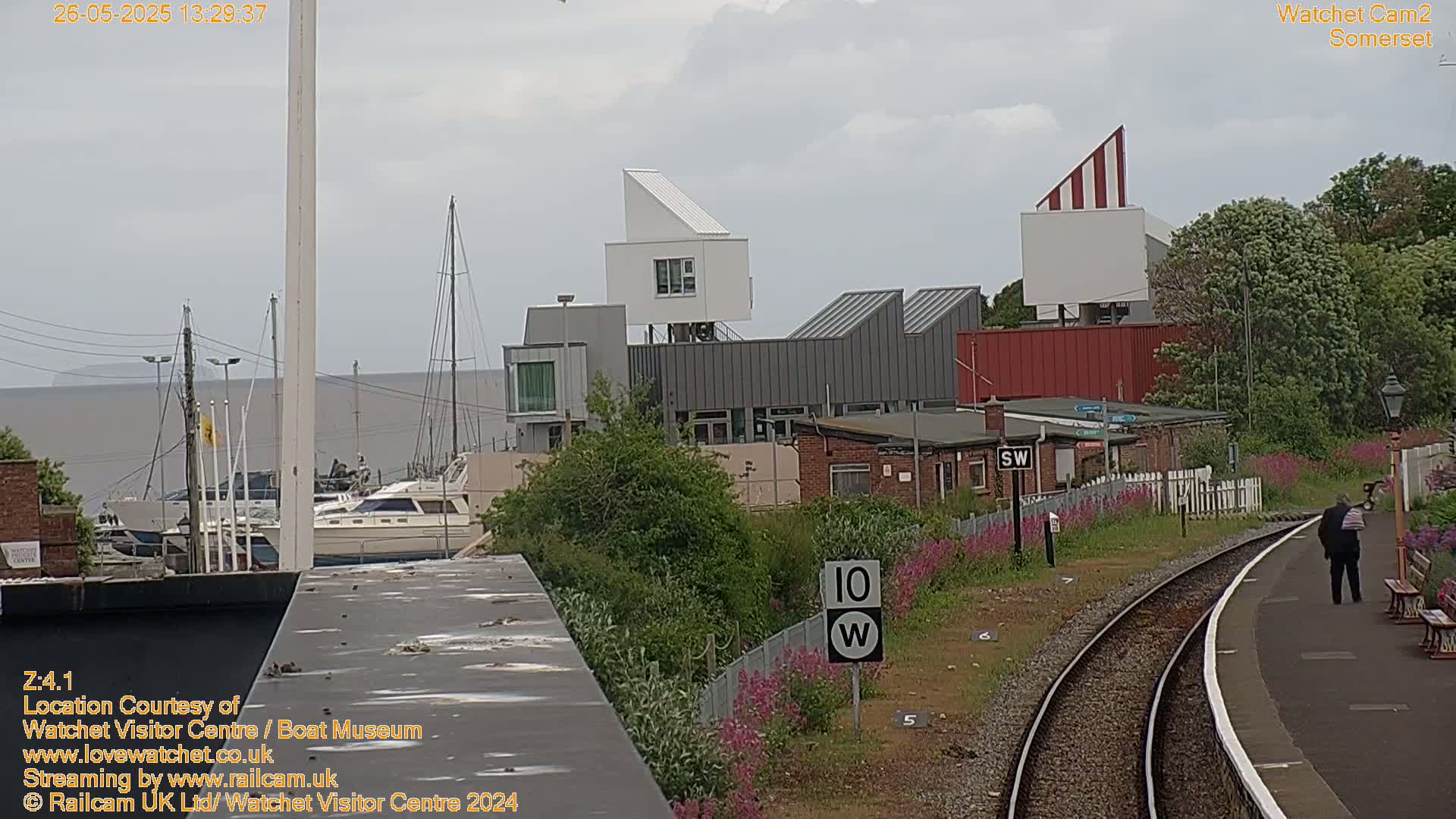 A marina with boats, modern buildings, and a railway line is visible under an overcast sky.