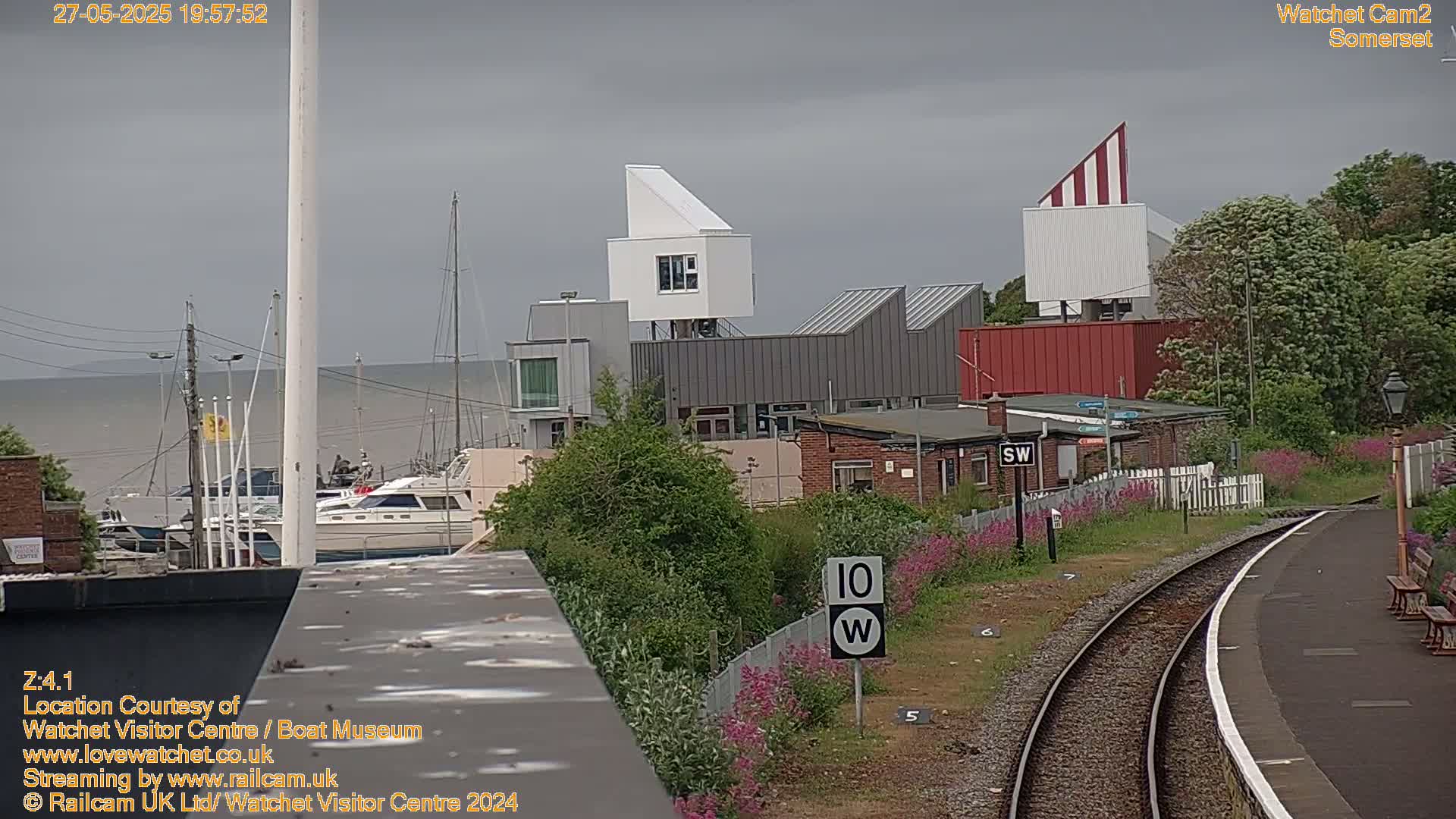 A view of a harbor with boats, modern buildings, and a railway track under an overcast sky.