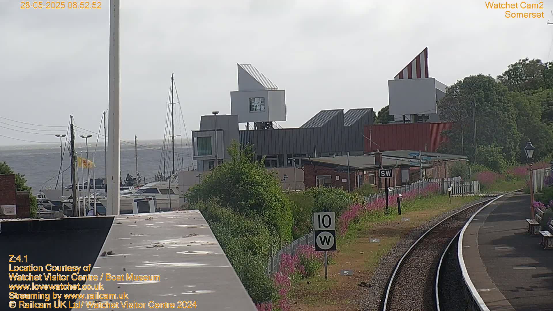 A view of a harbor with boats, modern buildings, and a railway track under an overcast sky.
