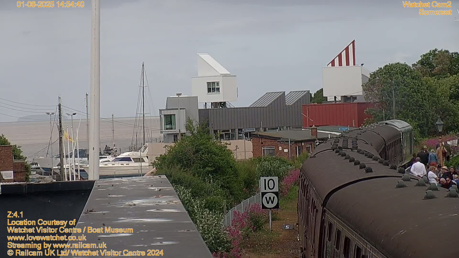 A train approaches a waterfront area with modern buildings under an overcast sky.