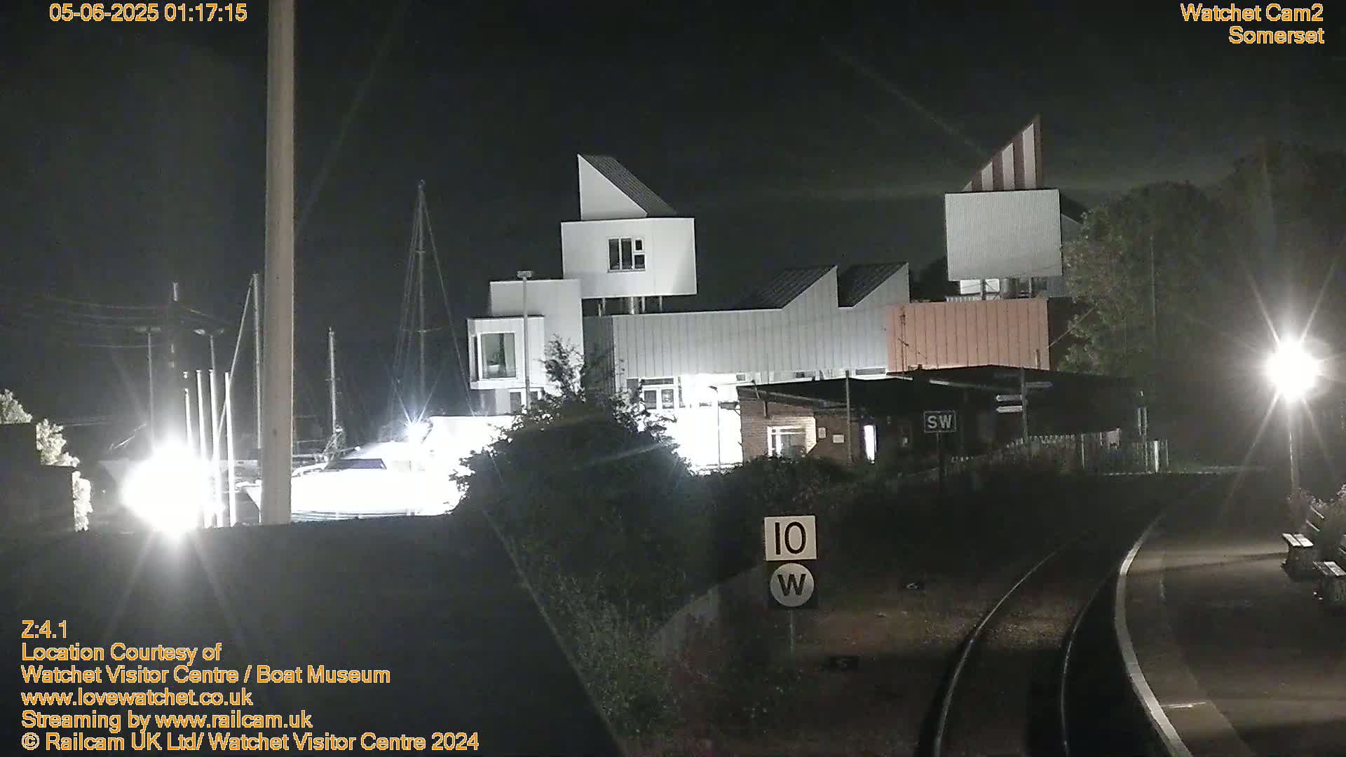 A modern, multi-level building is illuminated at night near a train track, under a dark sky.