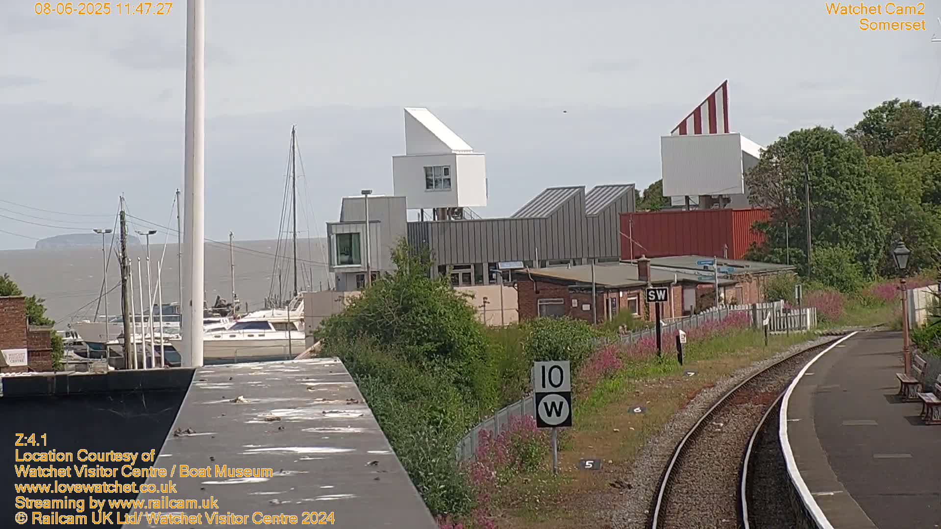 A view of a harbor with boats, modern buildings, and a train track on a sunny day.