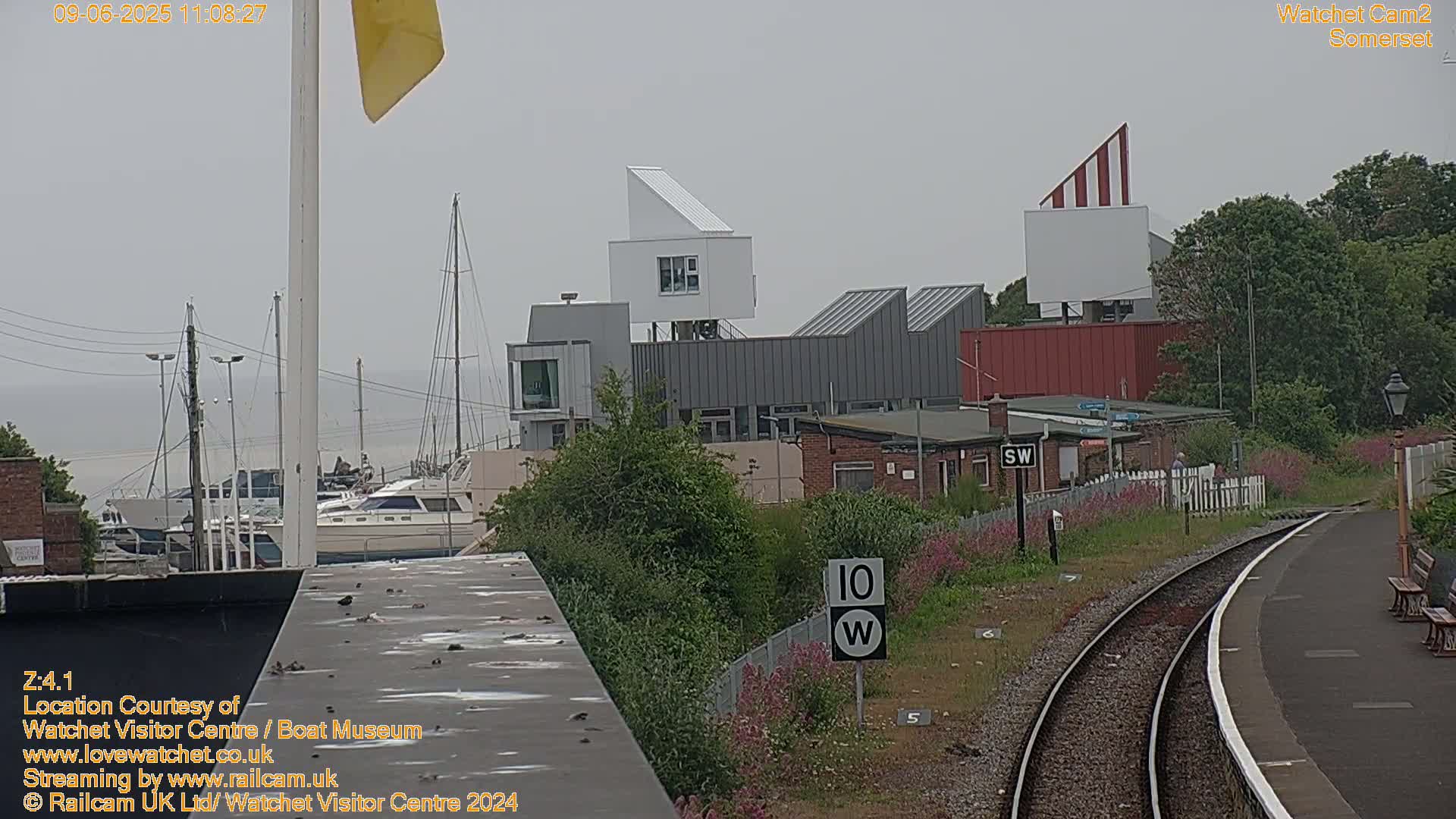 A hazy view of a harbor with boats, modern buildings, and train tracks on an overcast day.