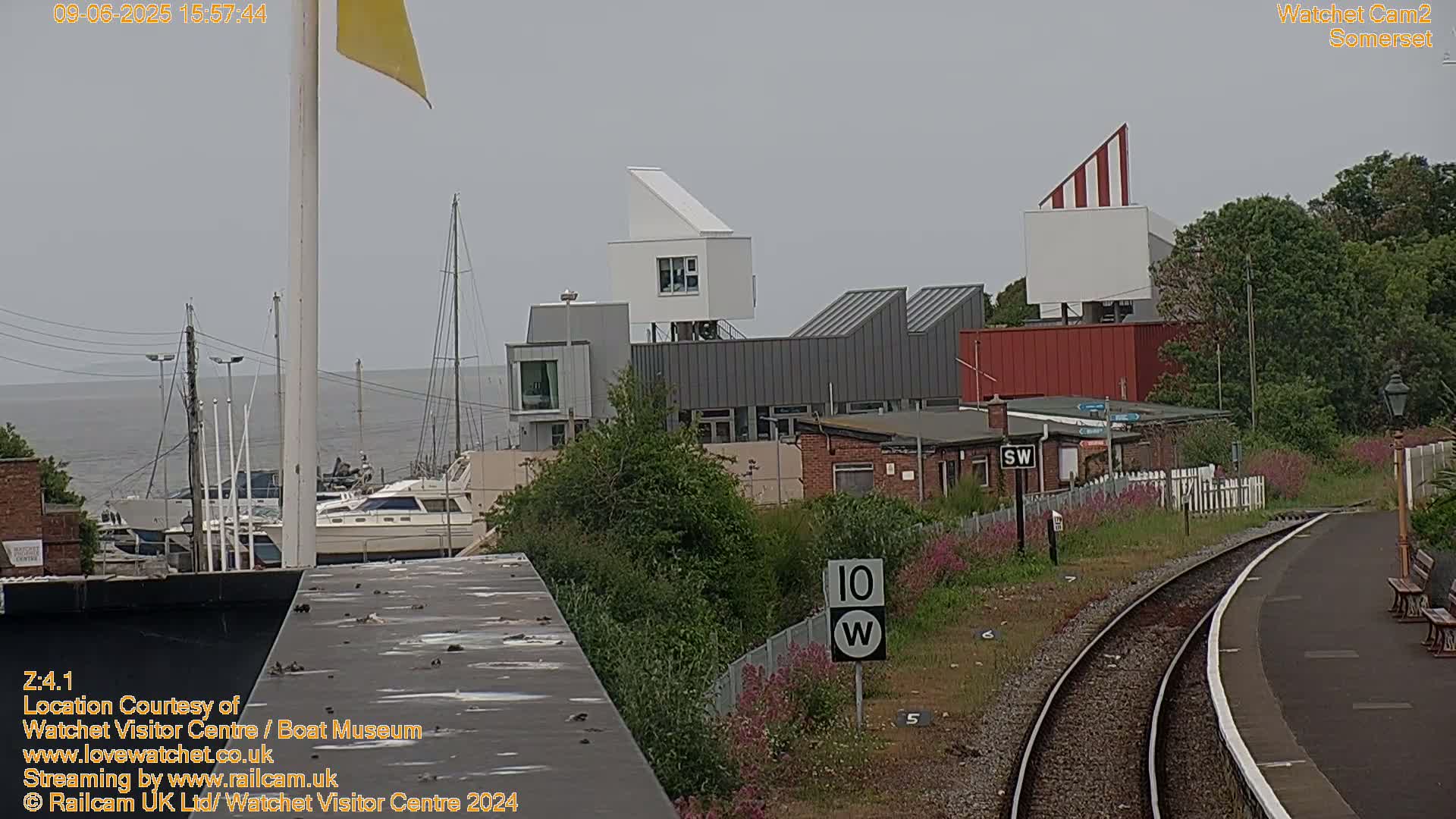 A view of a harbor with boats, modern buildings, and a train track on an overcast day.