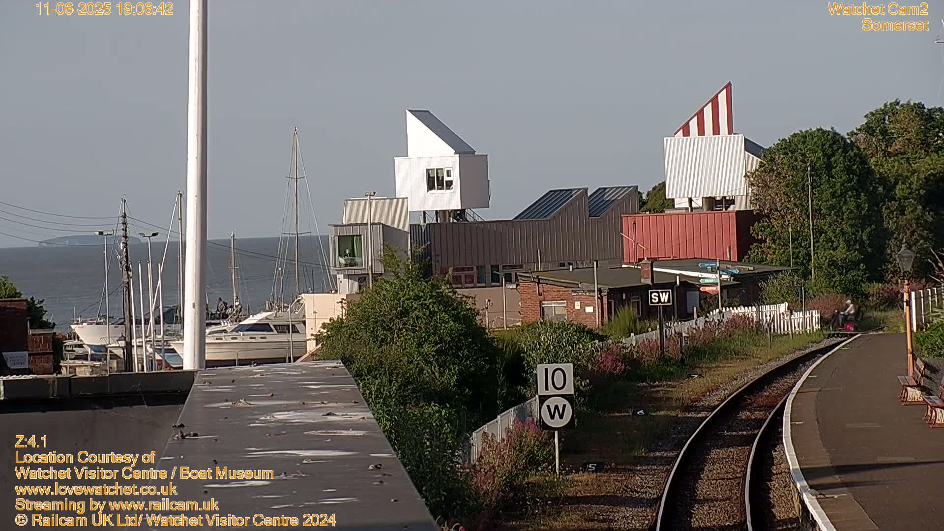 A sunny view of a harbor with boats, modern buildings, and a railway platform.