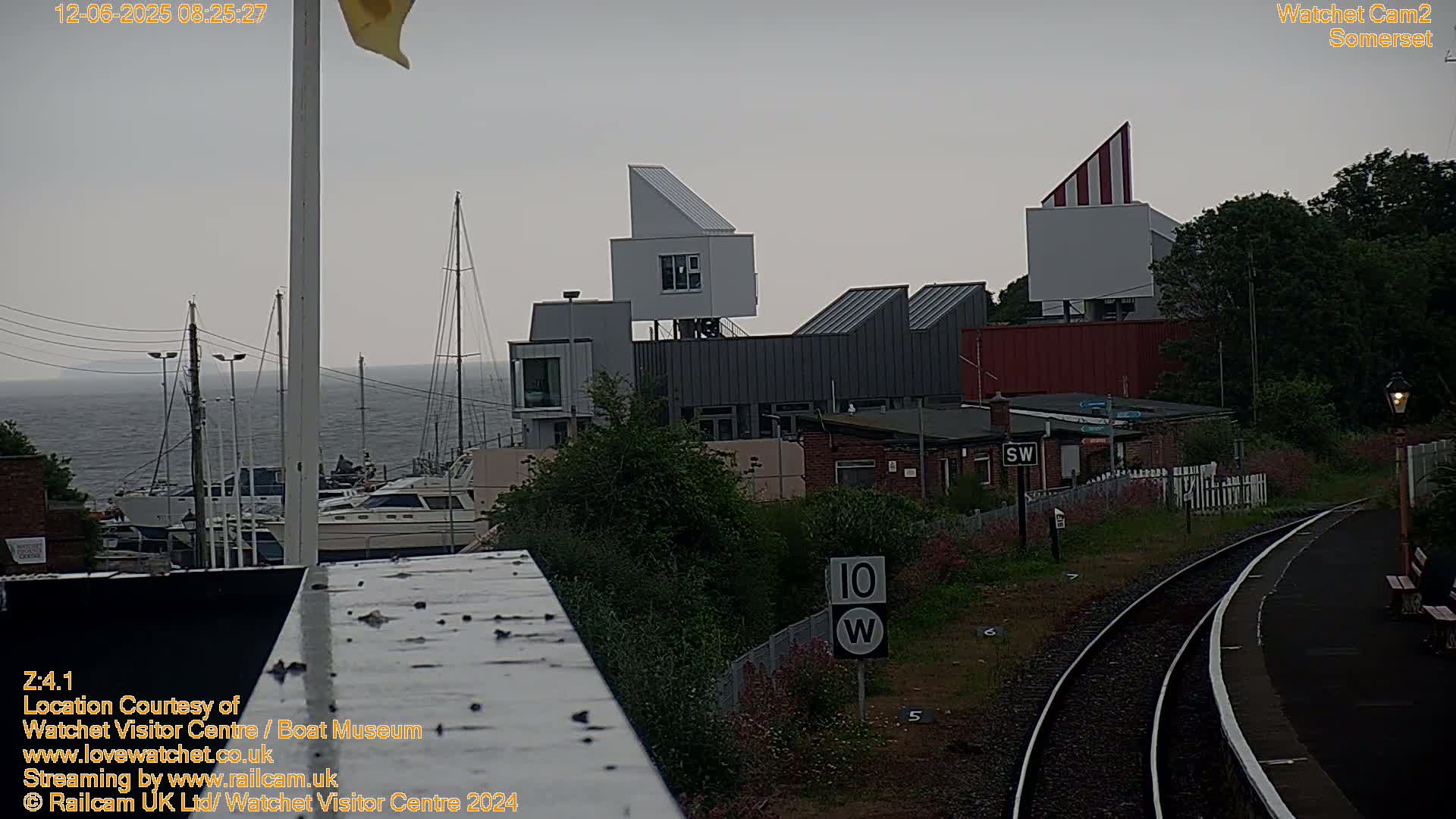 A gray, overcast day reveals a harbor with boats, a modern building complex, and railway tracks leading to a station.