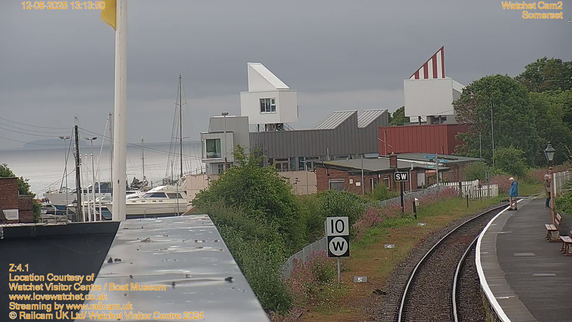 A seaside town with modern buildings near a train station and harbor, under an overcast sky.