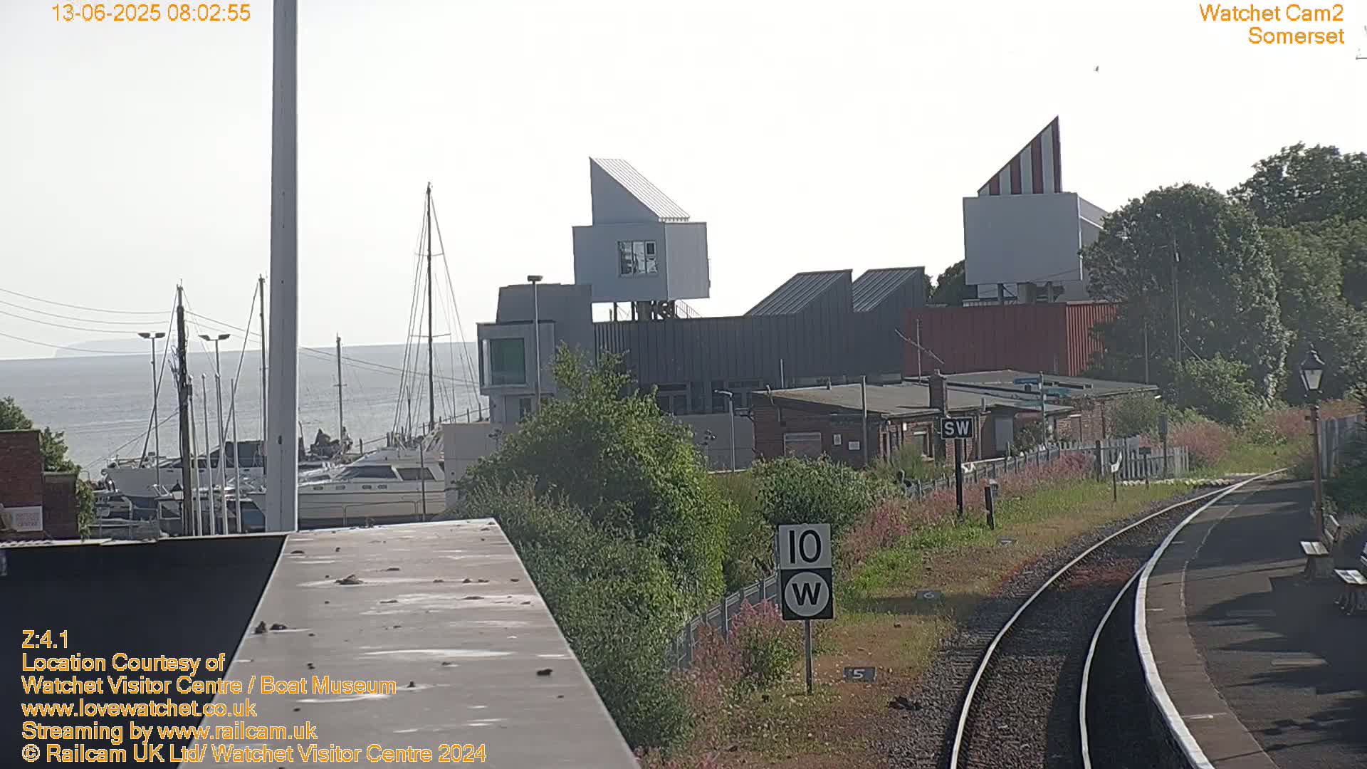 A view of a harbor with boats, modern buildings, and train tracks on a partly cloudy day.