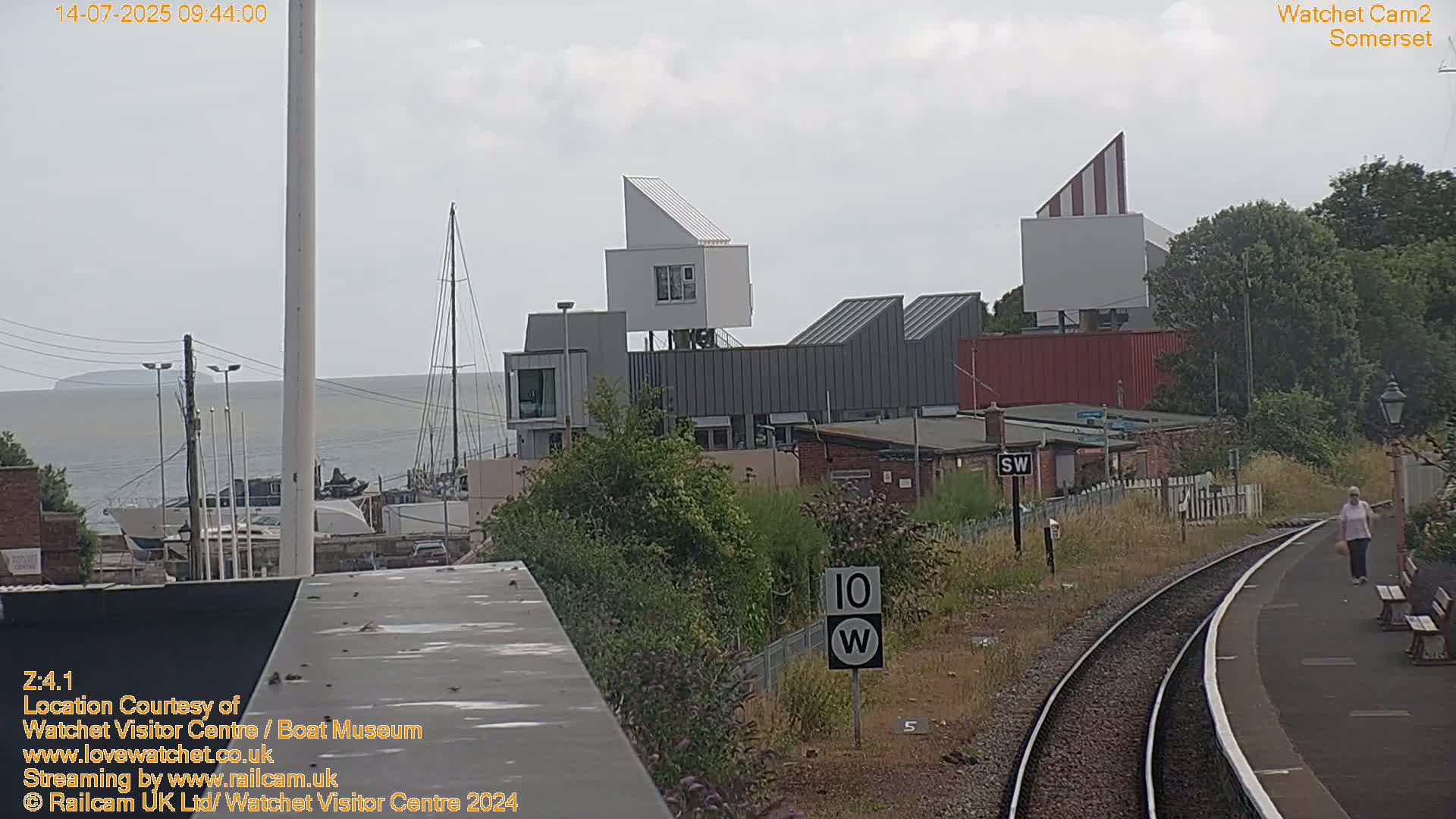 A view of a waterfront town with modern buildings, a body of water, and a train track on an overcast day.