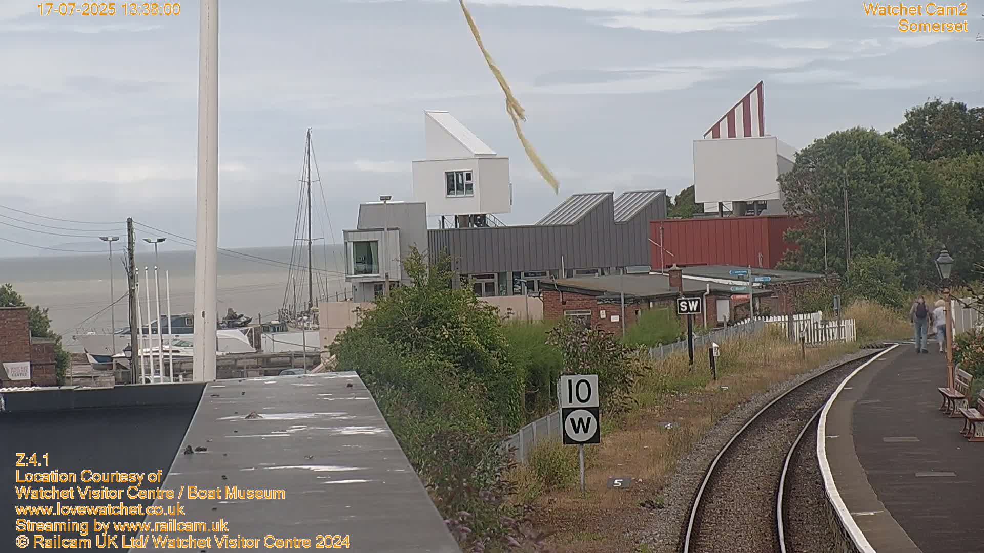 A view of a waterfront town with modern buildings, a body of water, and a train track on an overcast day.