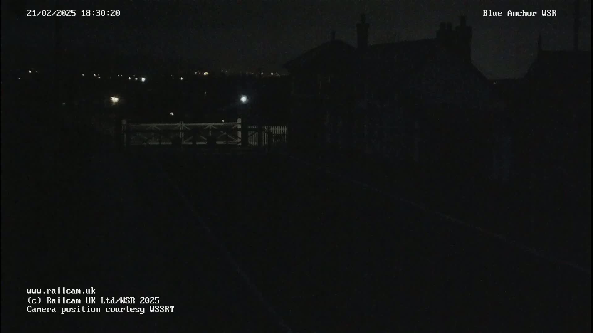 A nighttime view of a dark railway line and a dimly lit building under a clear night sky.