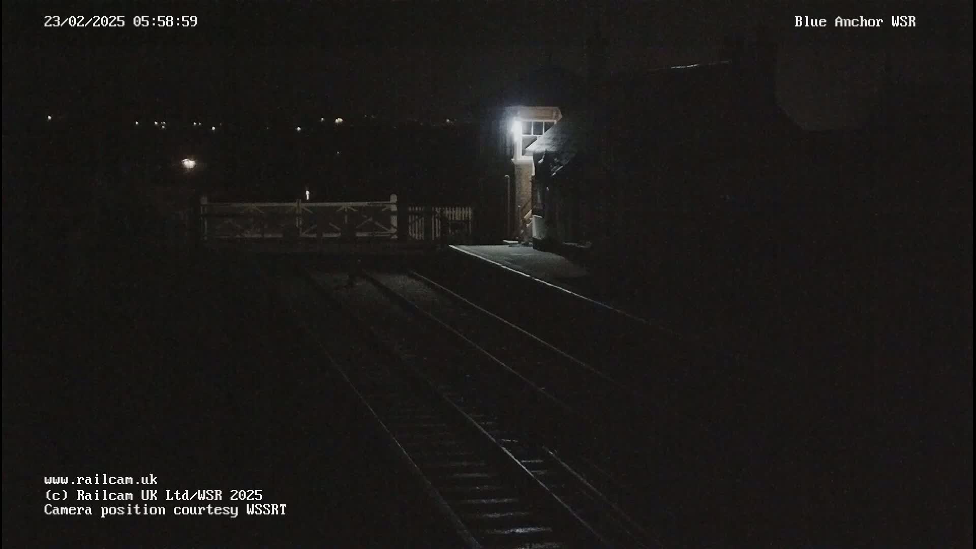 A dimly lit railway station platform at night is shown, with train tracks extending into the darkness.