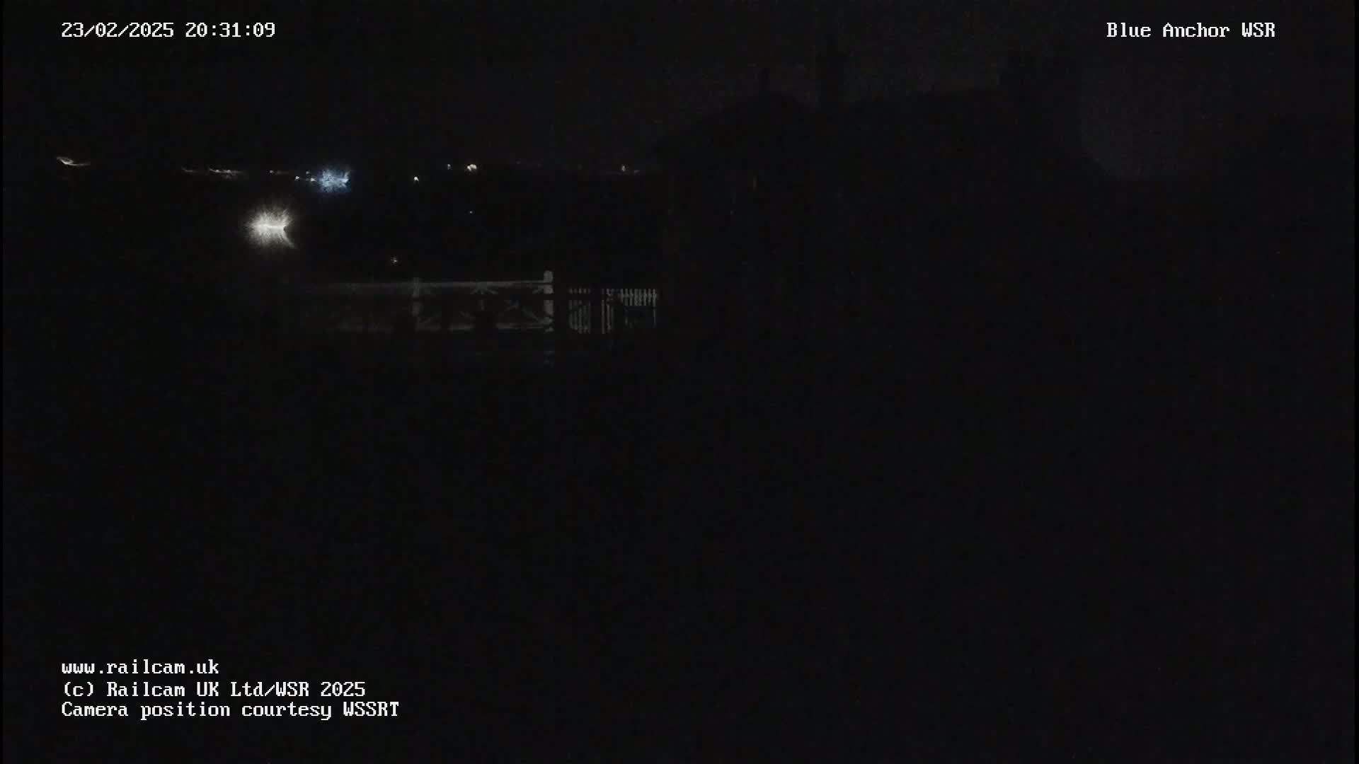 A nighttime, low-light view shows a dark landscape with faint lights in the distance.