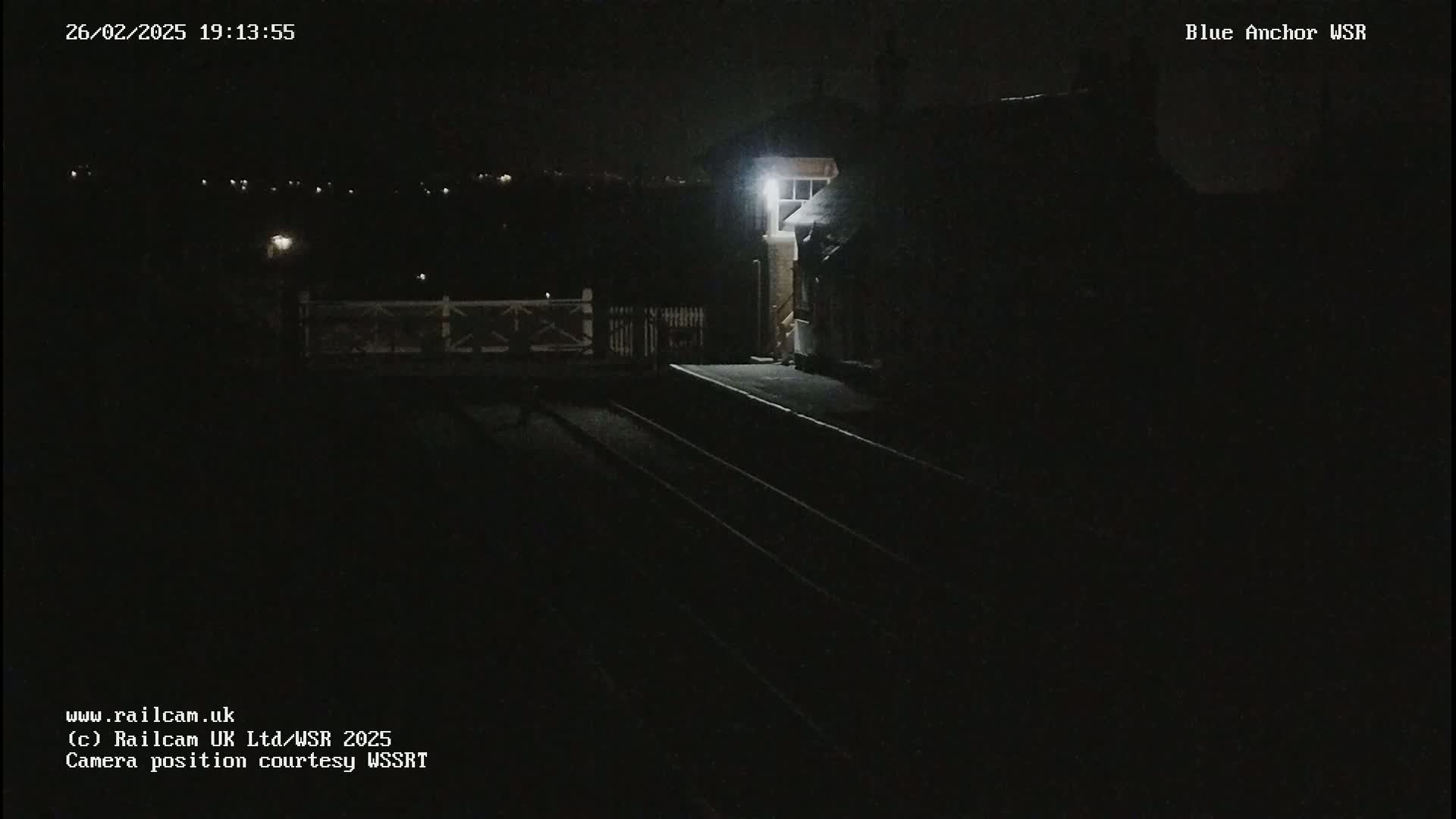 A dimly lit nighttime view of a train station platform and tracks under dark skies.