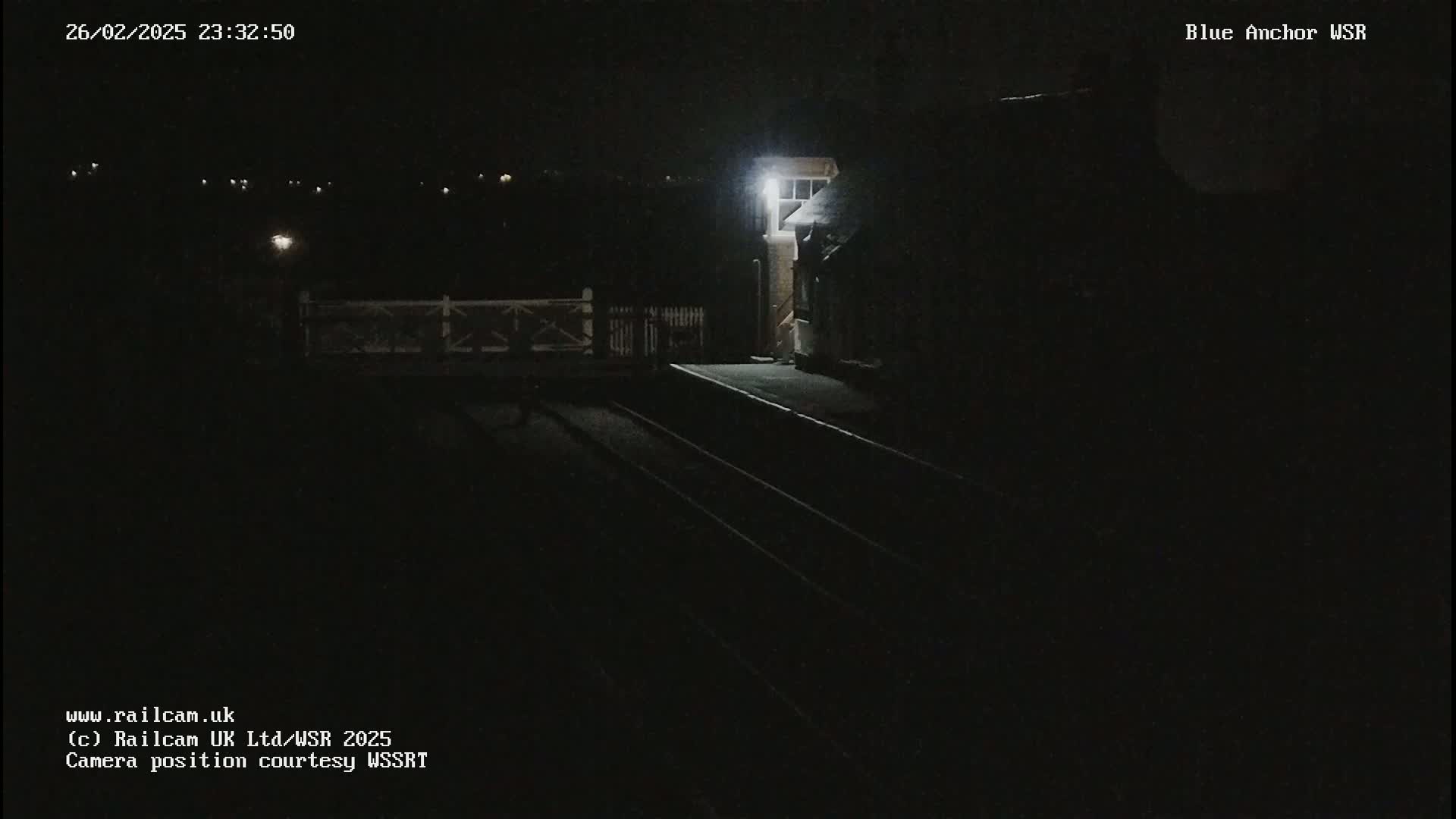 A dimly lit train platform and a small building are visible at night.