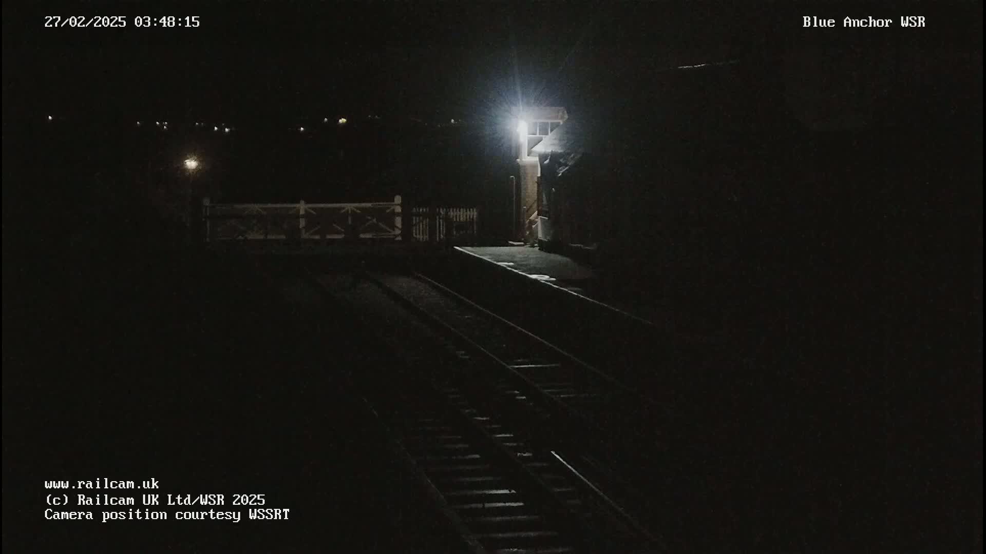 A nighttime view of a dimly lit train platform and railway tracks.