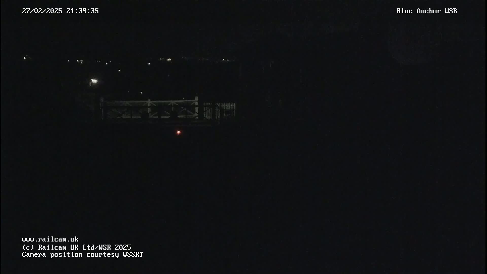 A nighttime, dark view of a bridge with faint lights in the distance.