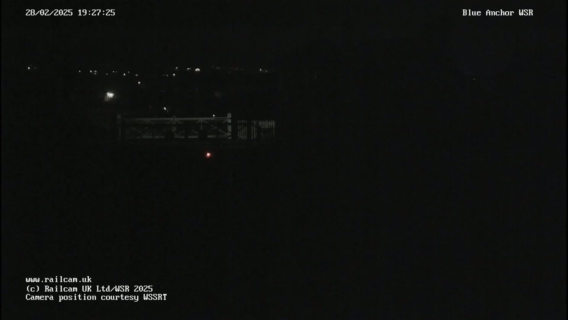 A nighttime, dark image shows a dimly lit bridge and distant lights in the background.