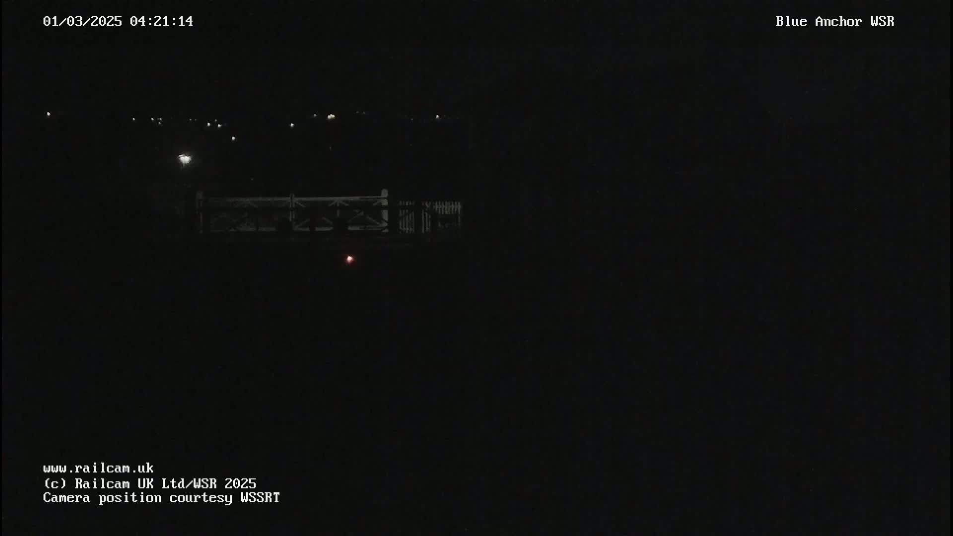 A dark, nighttime view of a bridge with distant lights visible.