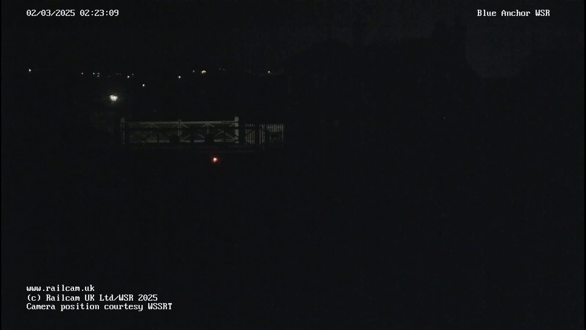 A nighttime, dark view of a bridge with a few distant lights visible under a clear, dark sky.