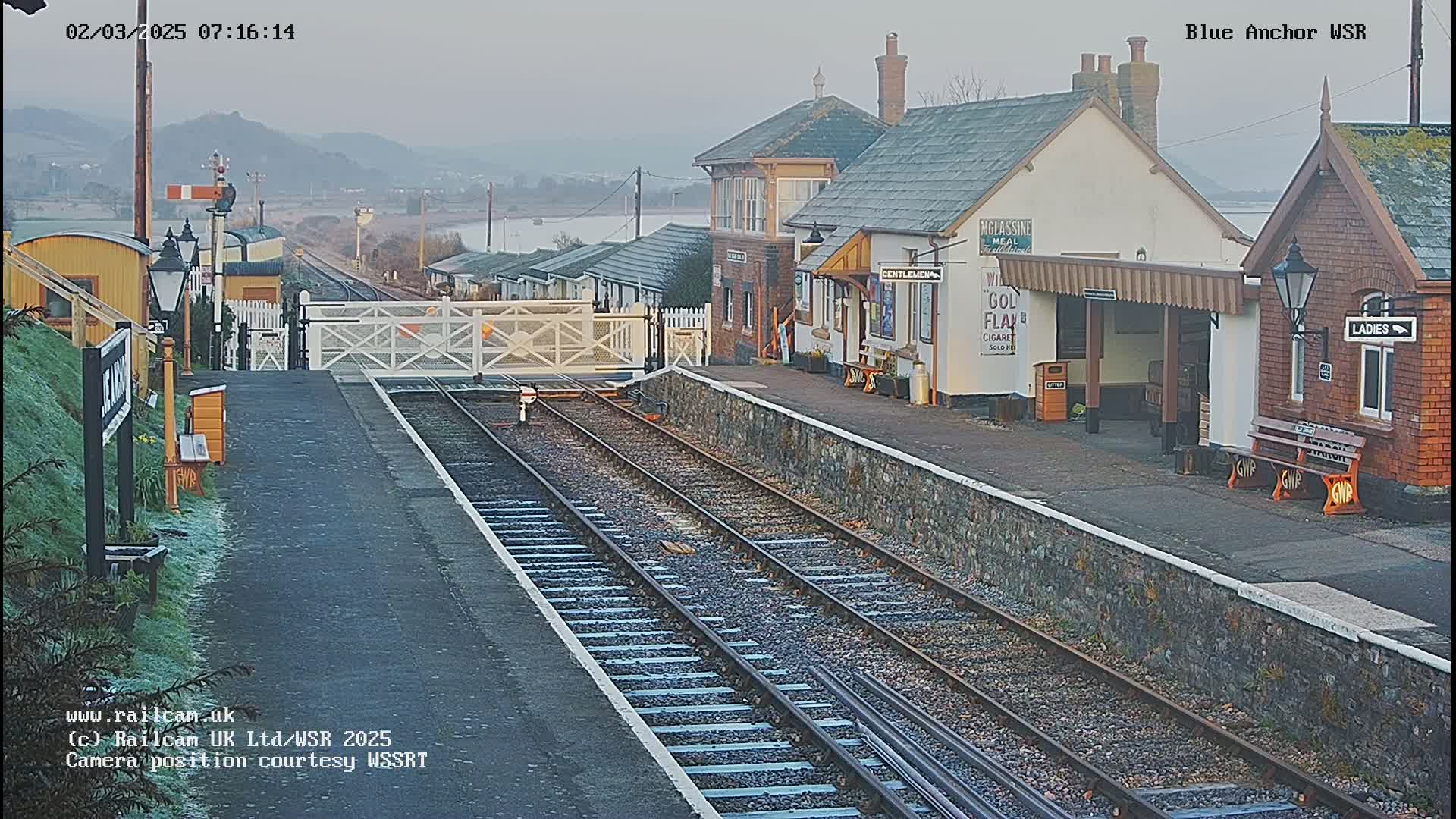 A railway station with two platforms and several buildings is seen on a misty morning.