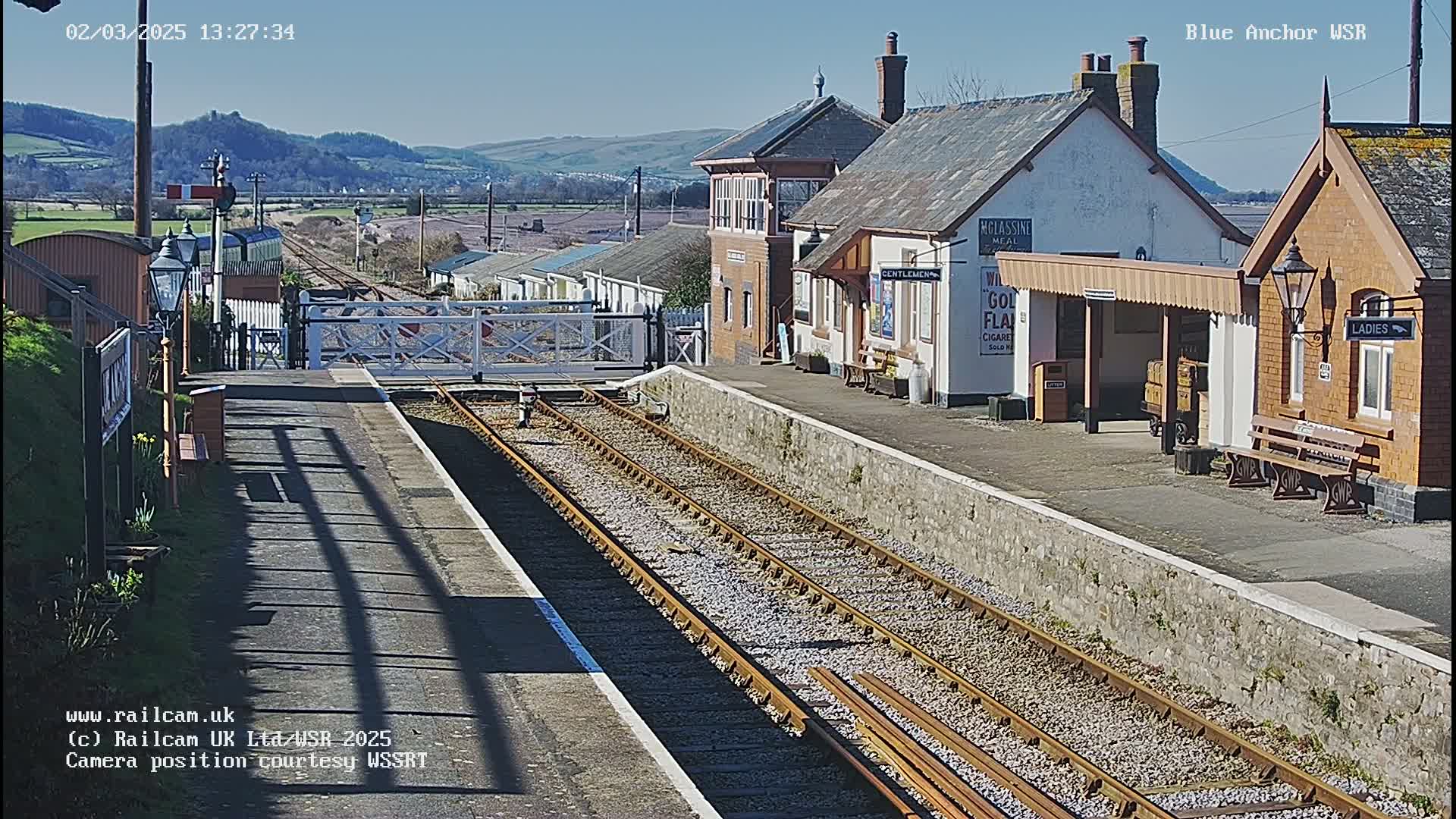 A sunny day at a railway station with multiple train tracks, a signal box, and several station buildings.