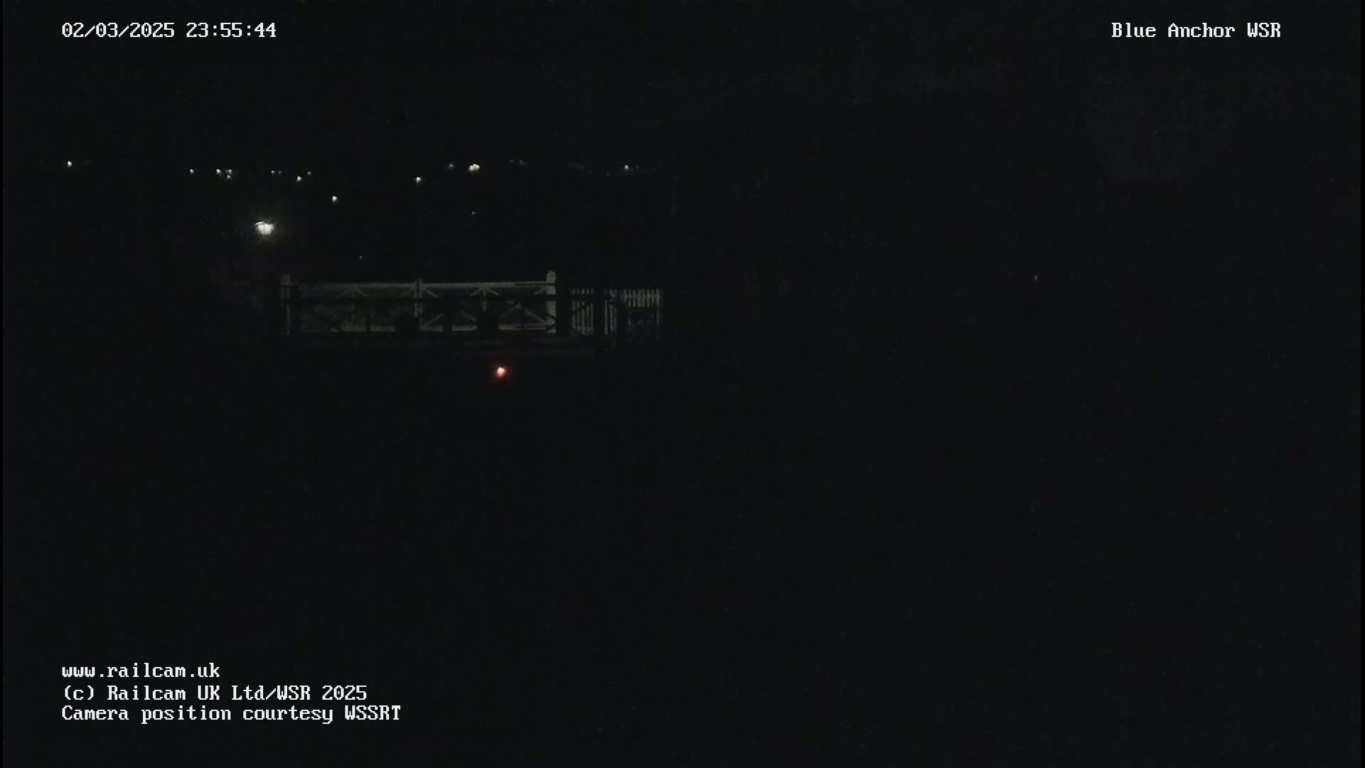 A dark nighttime scene shows a dimly lit bridge and distant lights.
