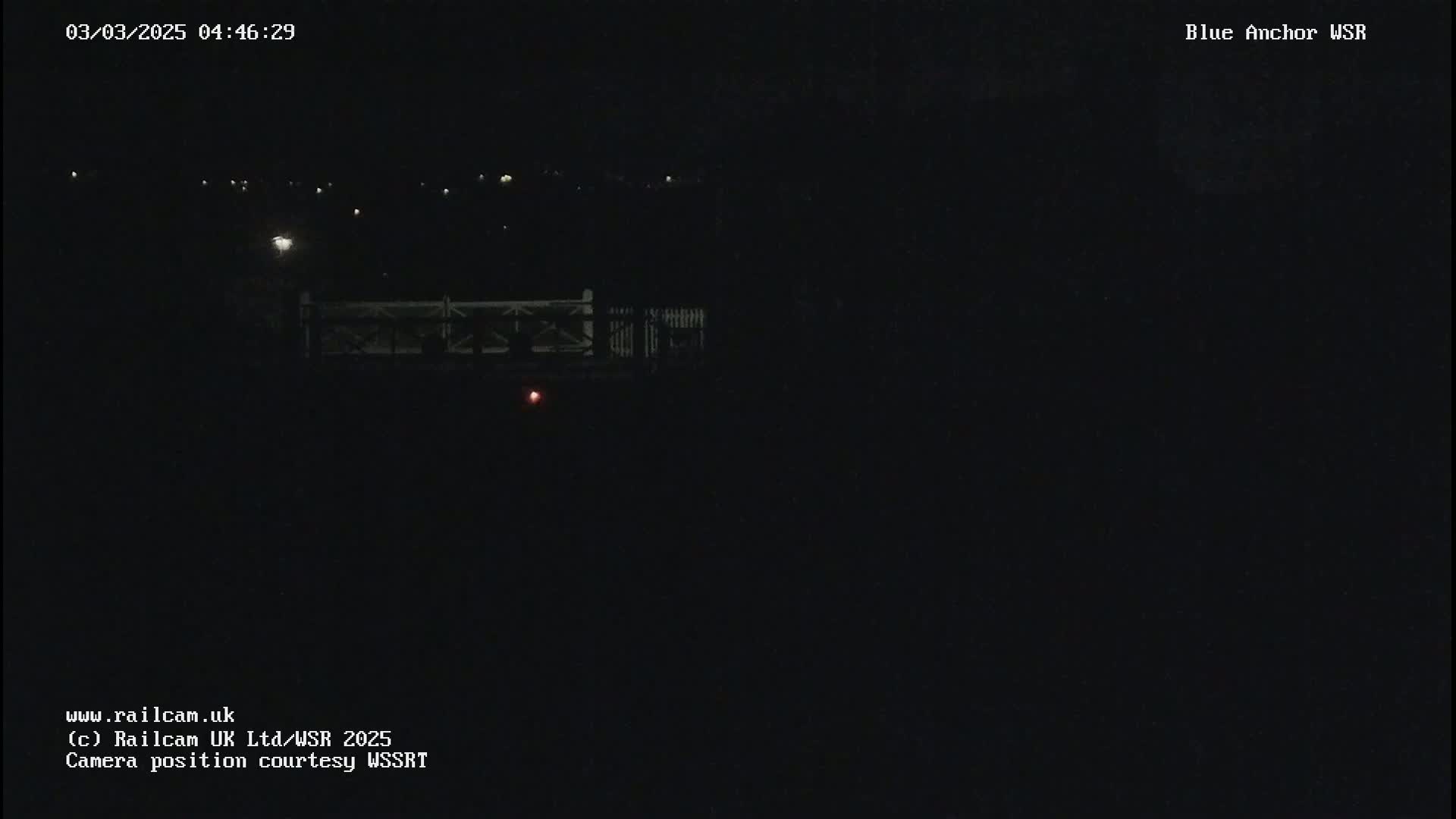A nighttime, dark view of a bridge with a few distant lights visible.