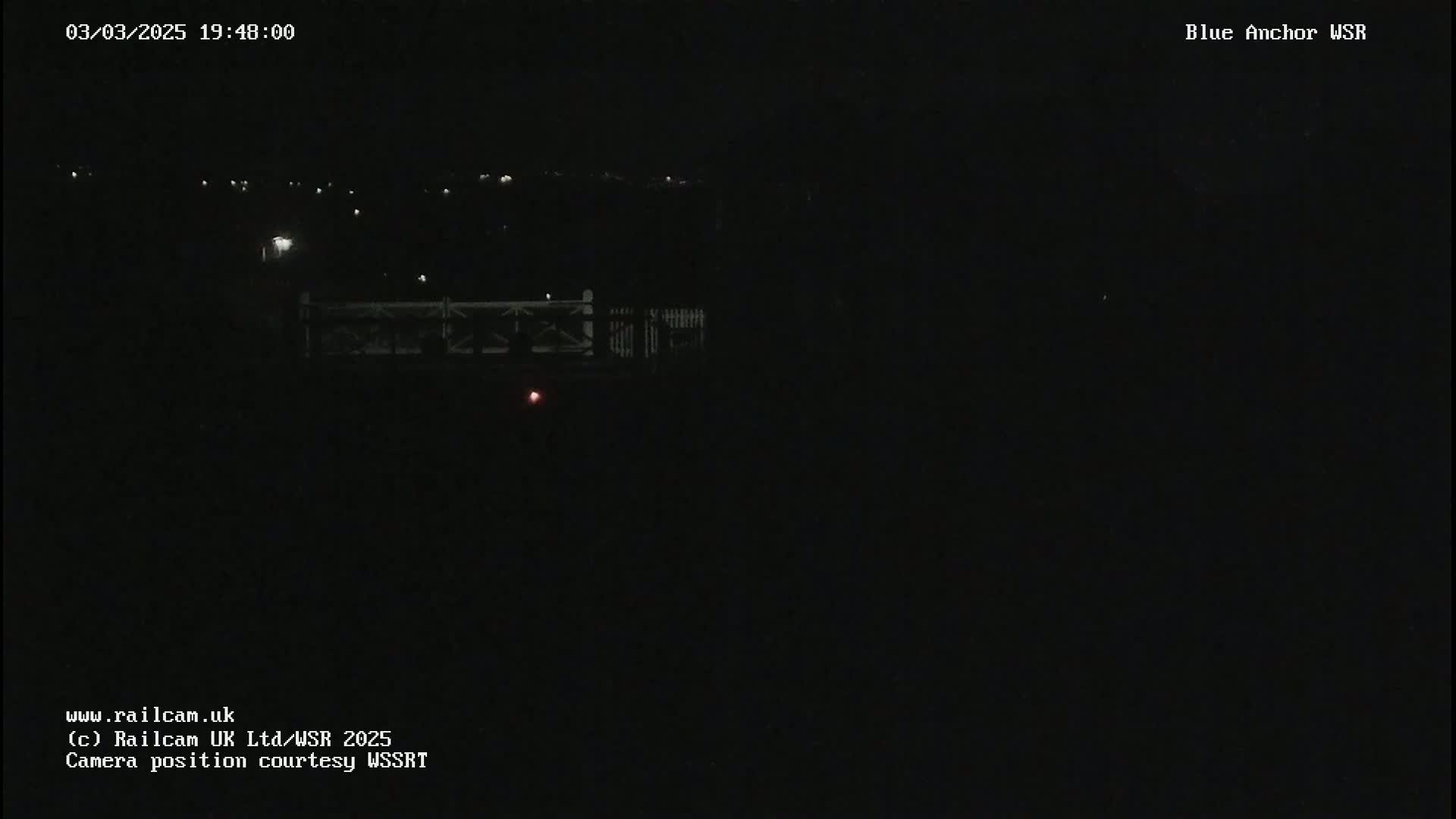 A dark, nighttime scene shows a dimly lit bridge and distant lights.