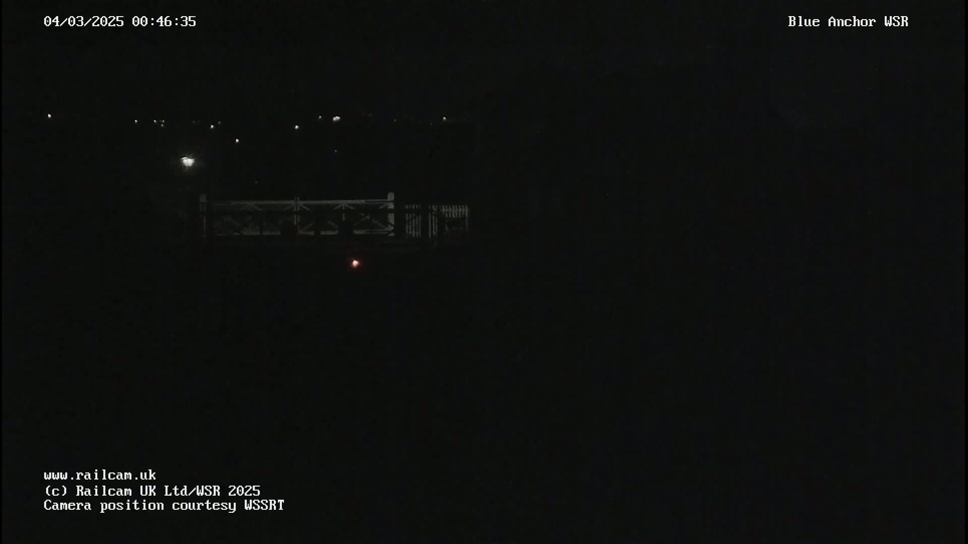 A nighttime, dark view of a bridge with faint lights in the distance.