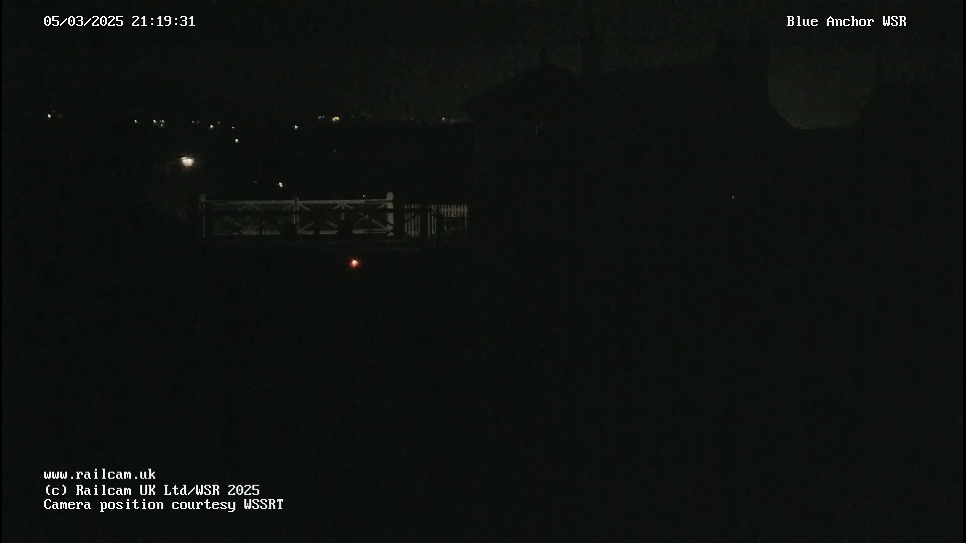 A dark nighttime scene shows a dimly lit bridge and building under a clear, dark sky.
