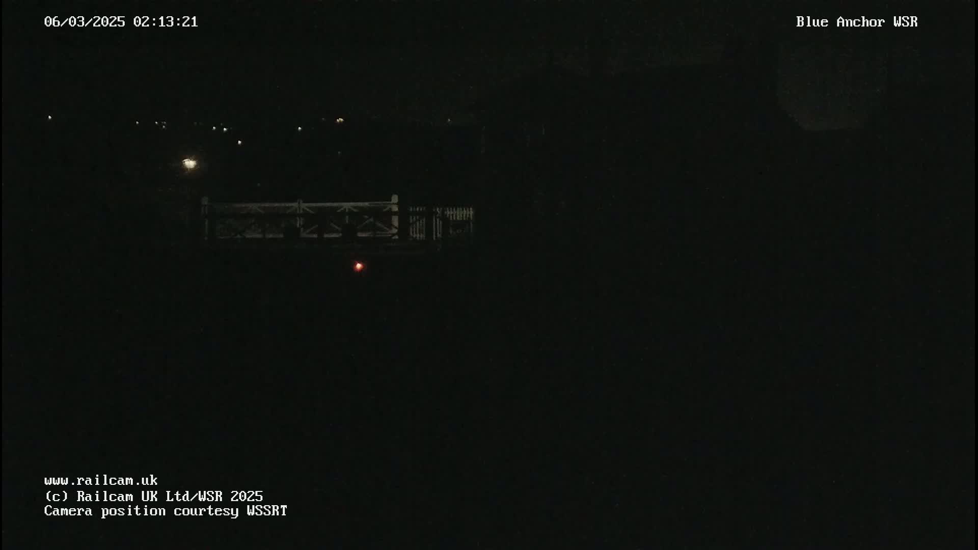 A nighttime, dark image shows a dimly lit bridge and a few distant lights.