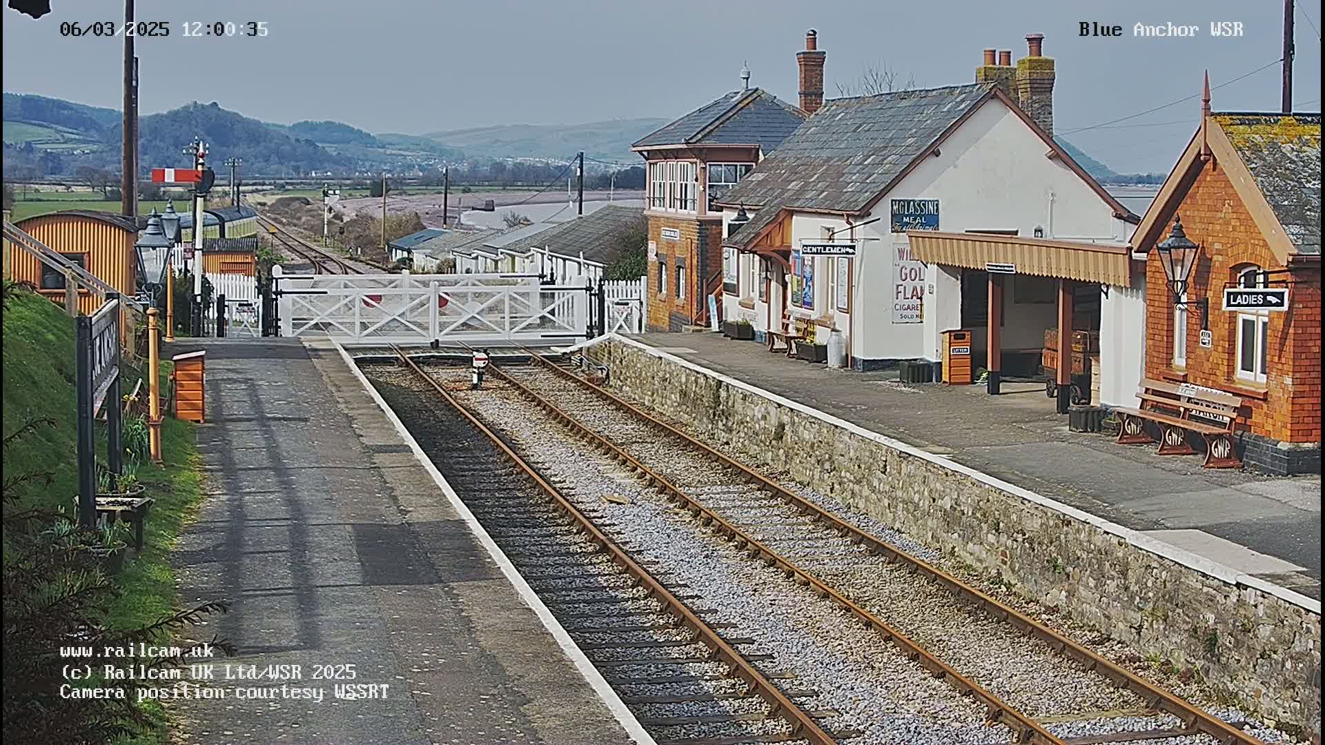 A train station with a signal gate down and two sets of train tracks, under a mostly clear sky.