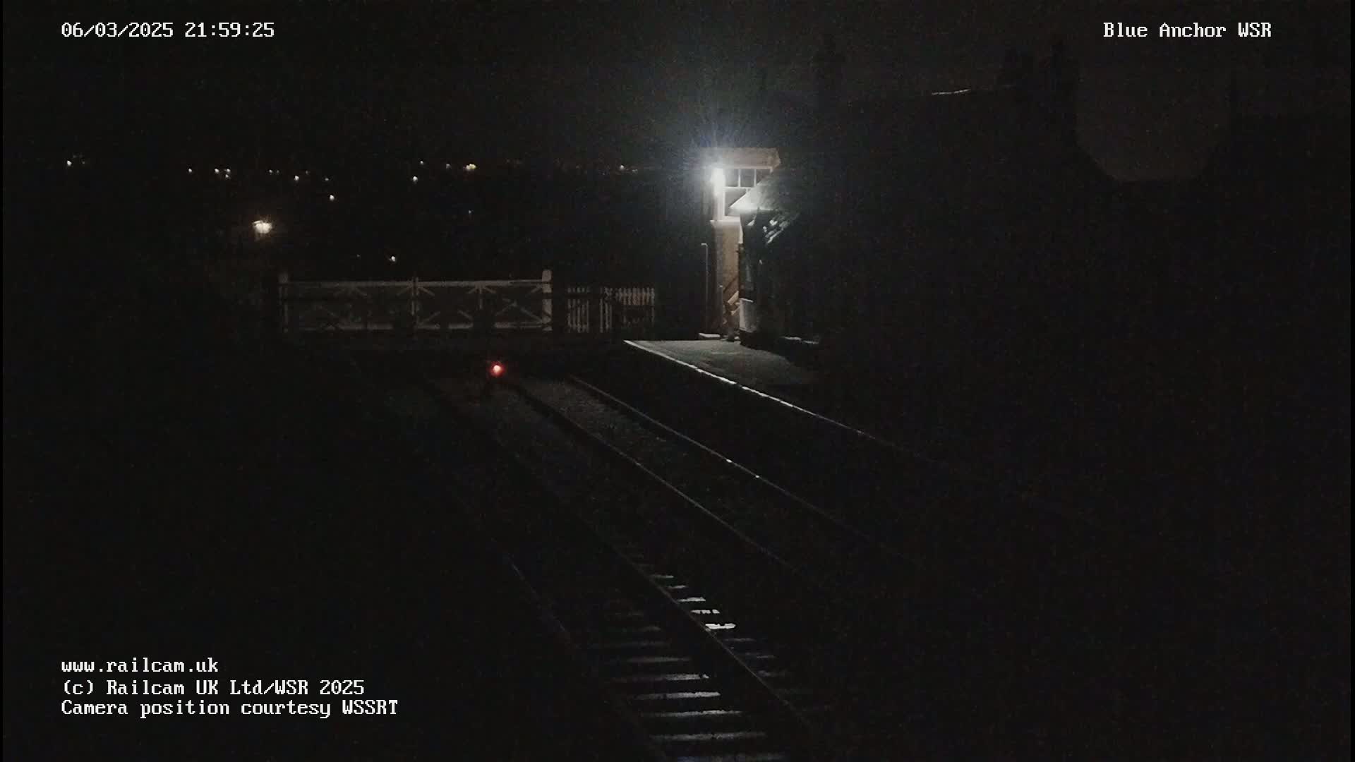 A nighttime view of a dimly lit train station platform with train tracks extending into the darkness.