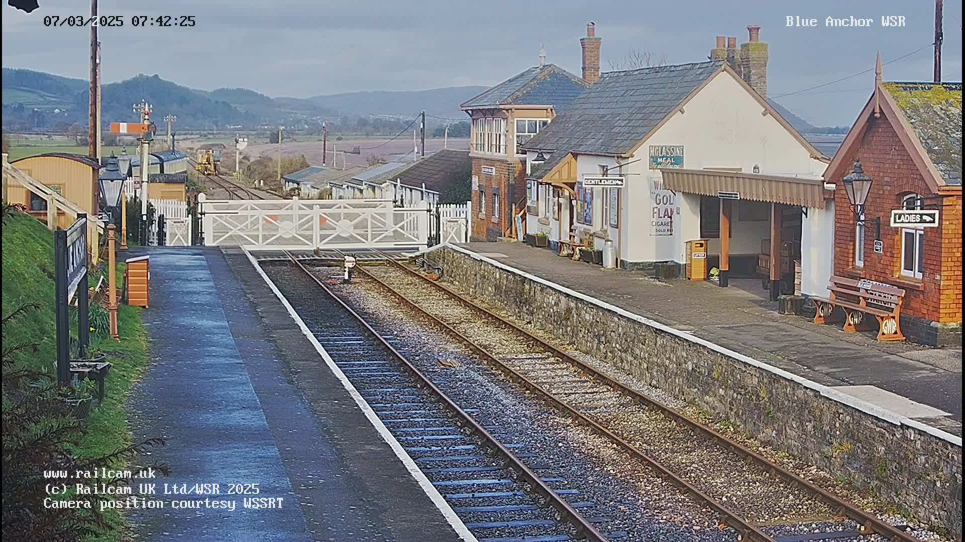 A train station with a signal box and two waiting shelters on a partly cloudy day.