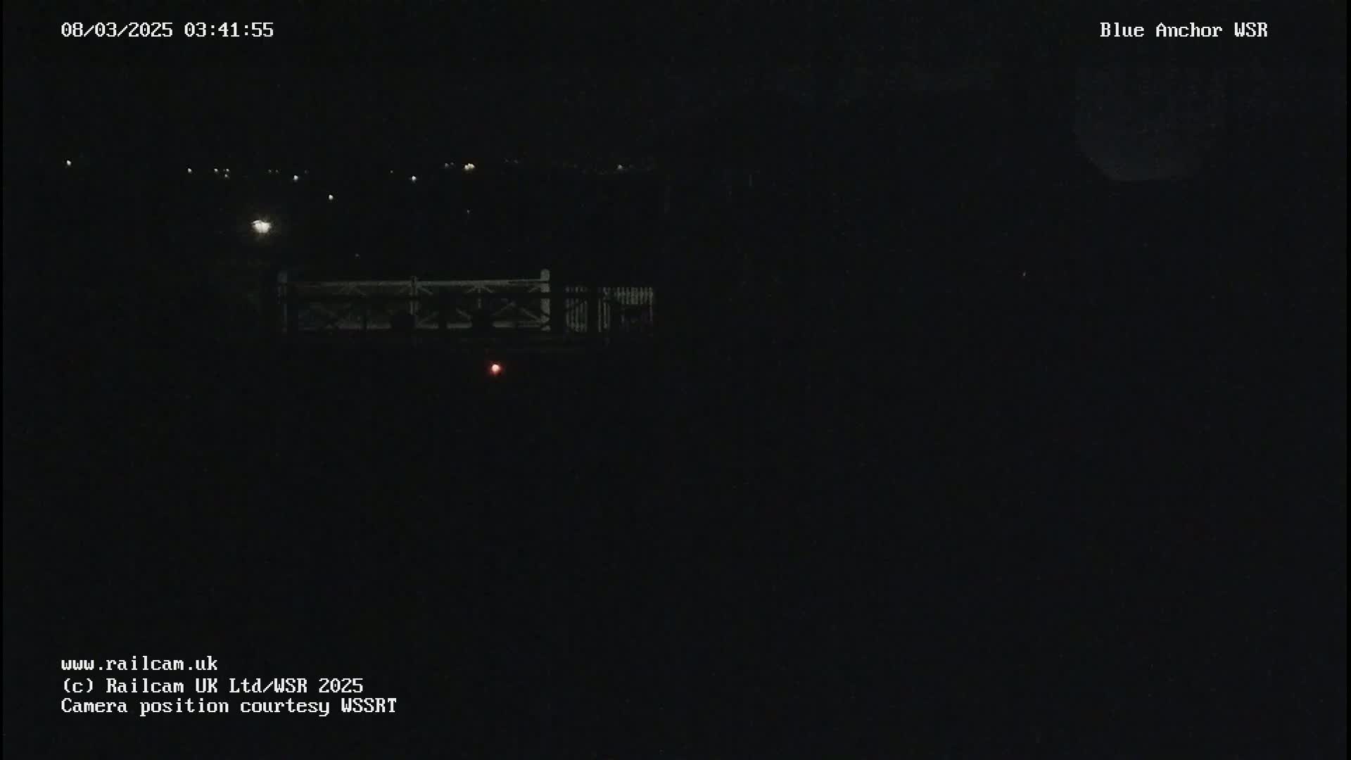 A nighttime, dark view of a bridge with a few distant lights visible.