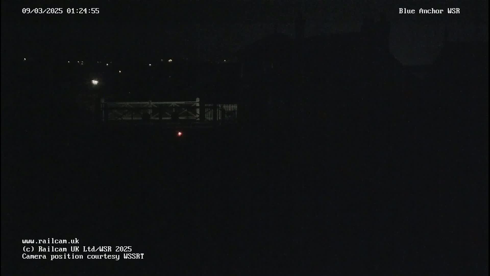 A nighttime, dark view of a bridge with a few distant lights visible.