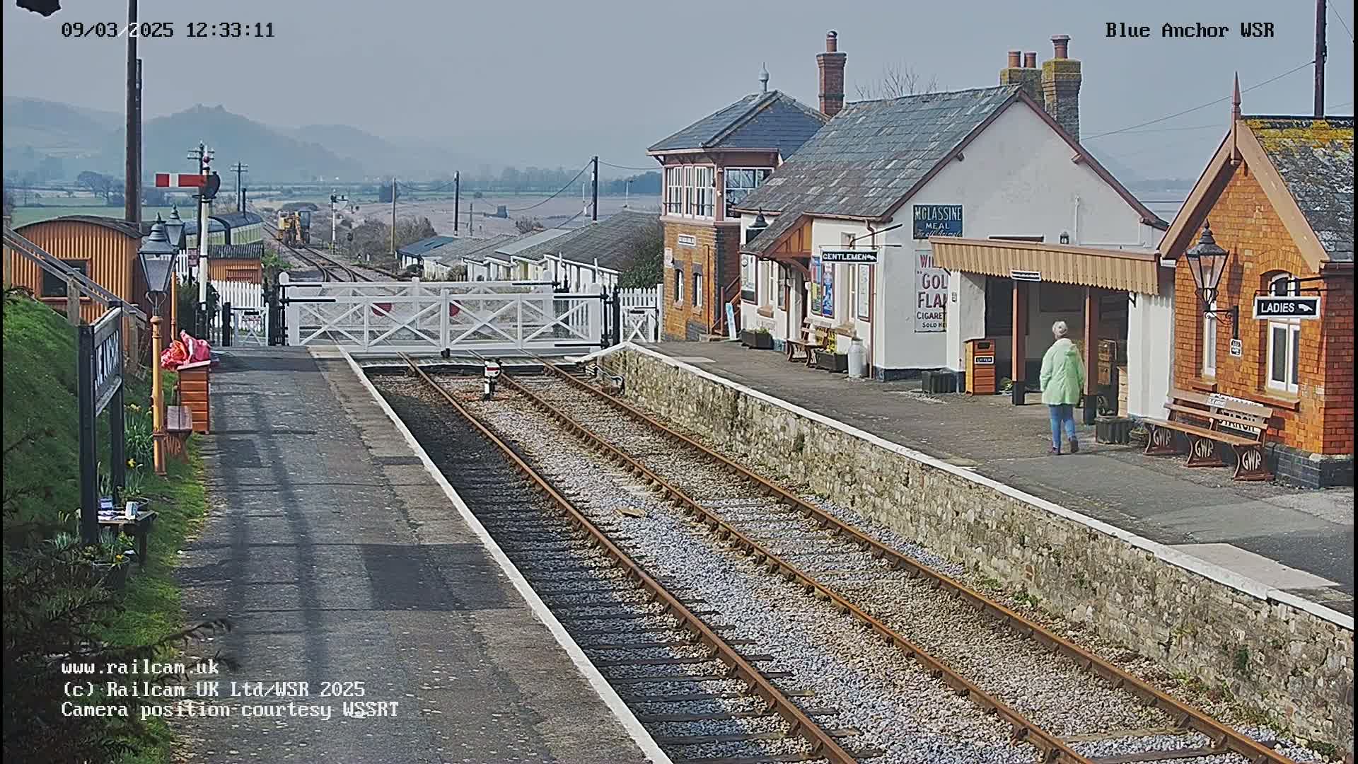 A train station with two platforms and a signal box, under a hazy sky.