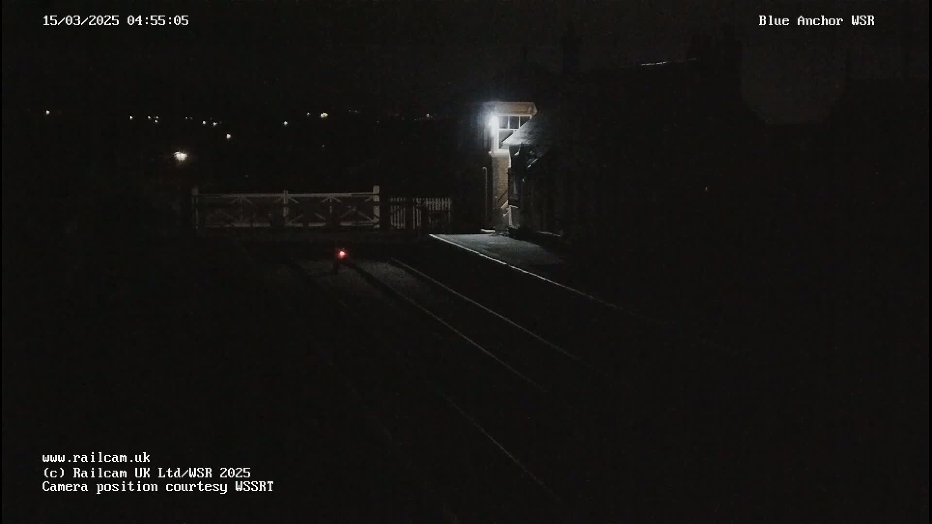 A dimly lit train station at night, showing empty train tracks and a building with a single light on.